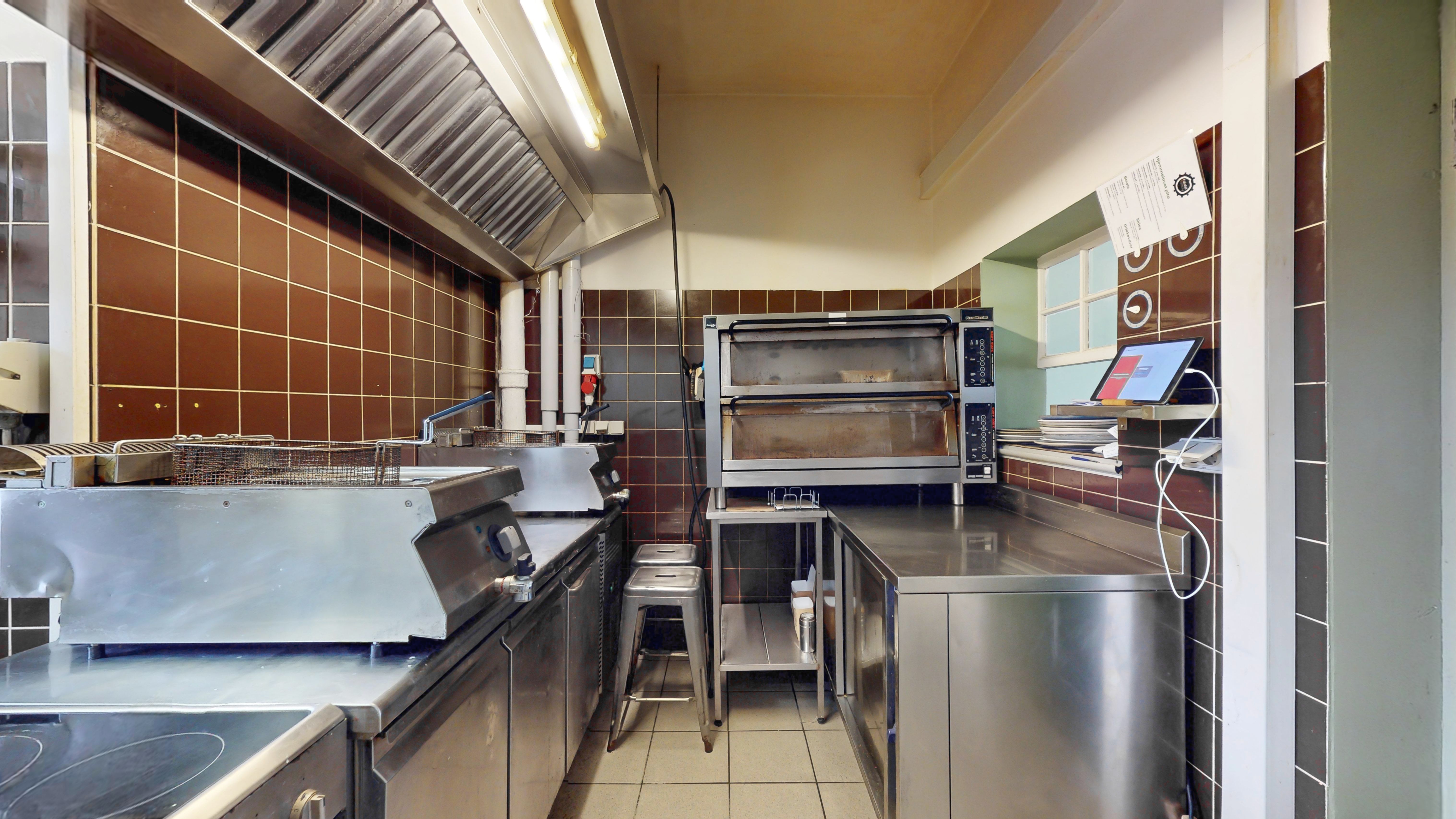 Moderne køkken med røde murfliser og flere køleskabe, to ovne og en bordplade med en tablet og en papirsuge.