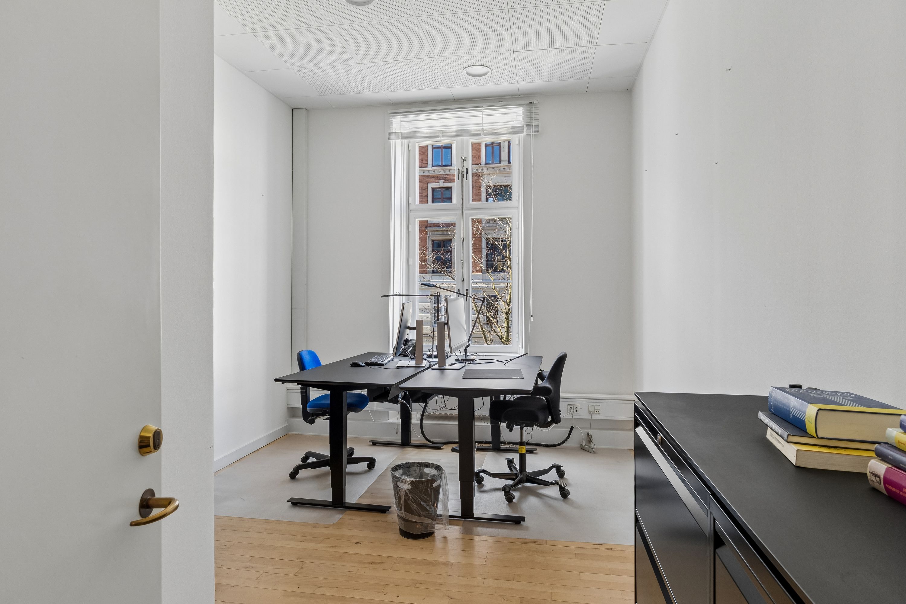 Kontor med moderne møbler, vinduer og to skriveborde med bærbare computere og en skraldspande i et lyst og velorganiseret arbejdsrum