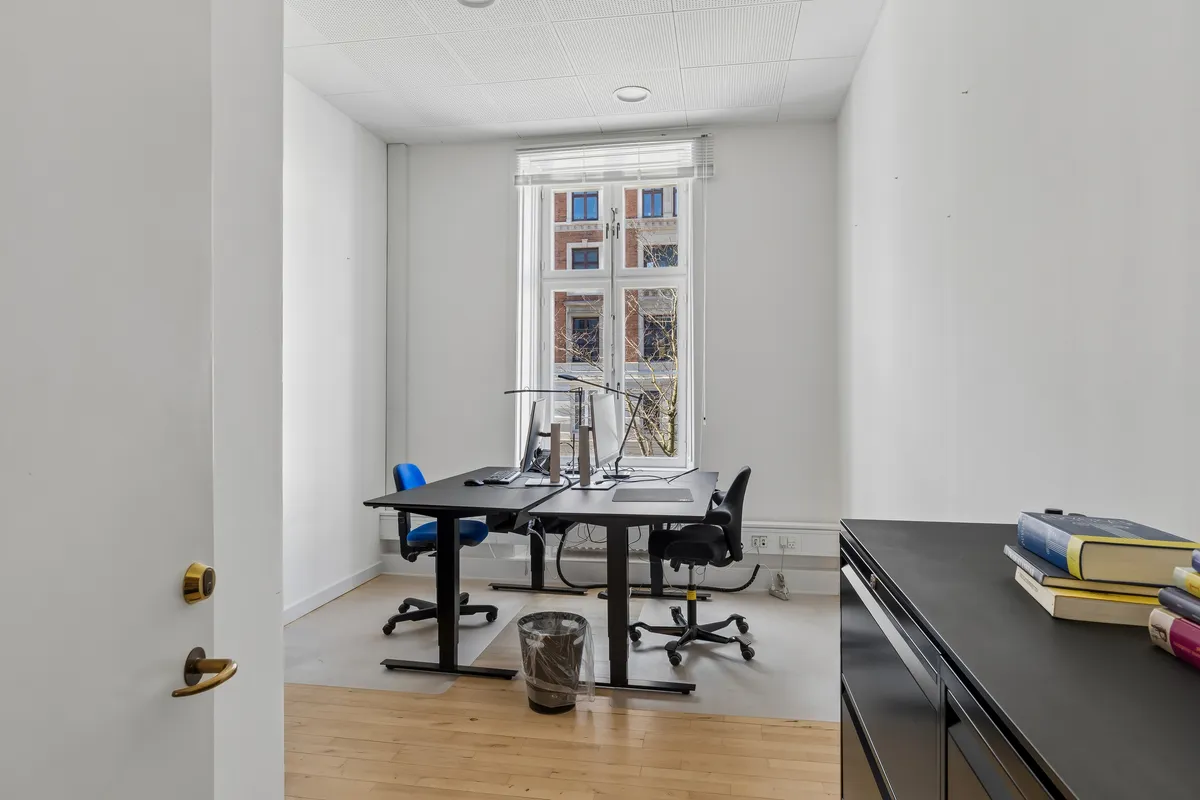 Kontor med moderne møbler, vinduer og to skriveborde med bærbare computere og en skraldspande i et lyst og velorganiseret arbejdsrum