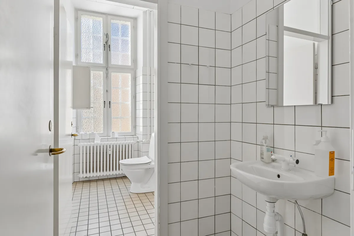 Rent og rent hvidt badeværelse med toilet, radiator og håndvask med håndsæbe og desinfektionsmiddel