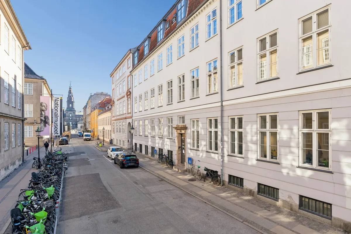 Kontorlokaller til leje i byens centrum, Ny Vestergade. Mange cykler parkeret langs gaden. Solskin på bygninger og røde tag. Søjler og grønne bænke.