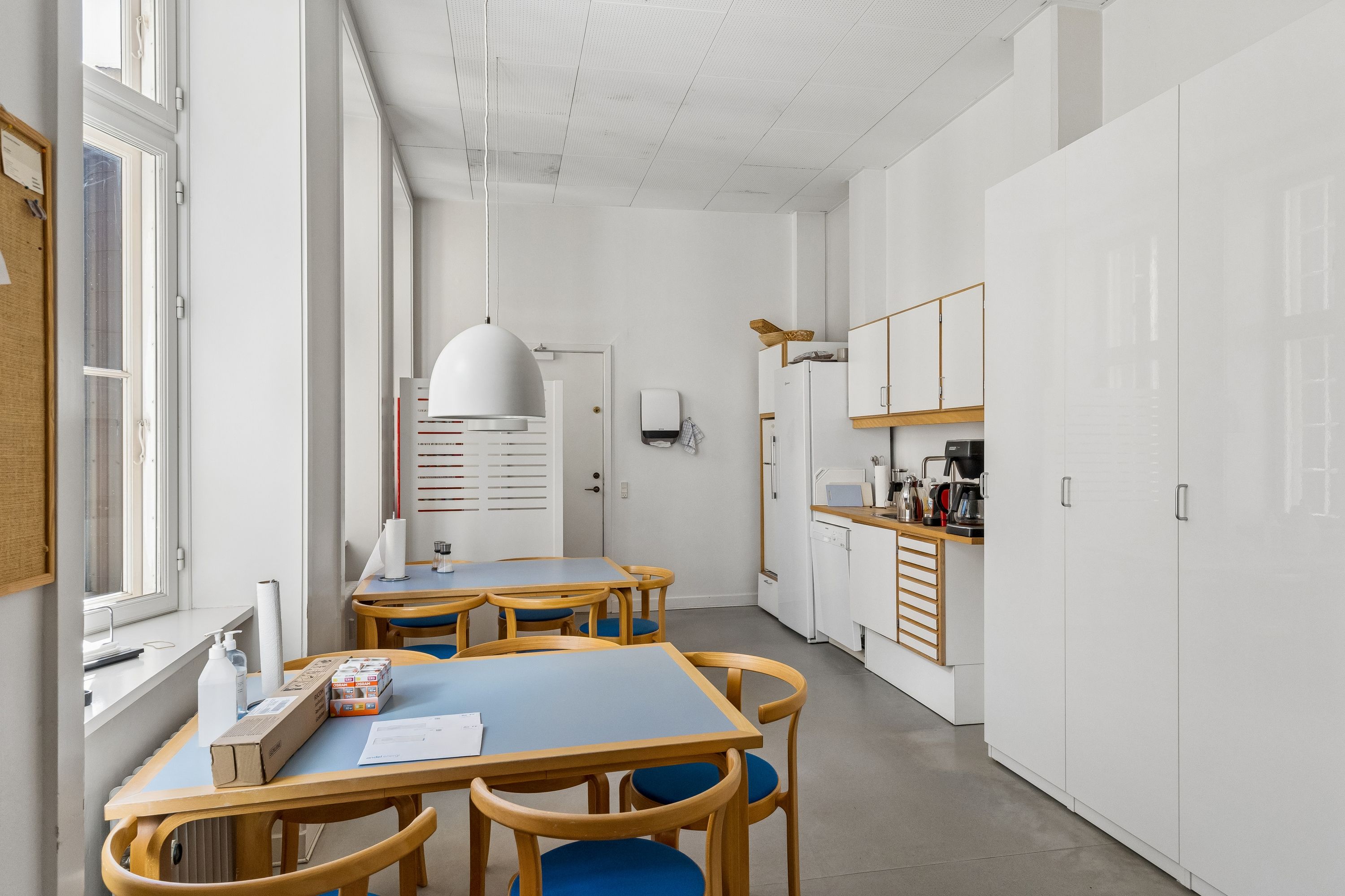 Kontorlokalien har moderne møbler, en stor glasdør, og en ren og minimalistisk design med hvide vægge og lyse lofter