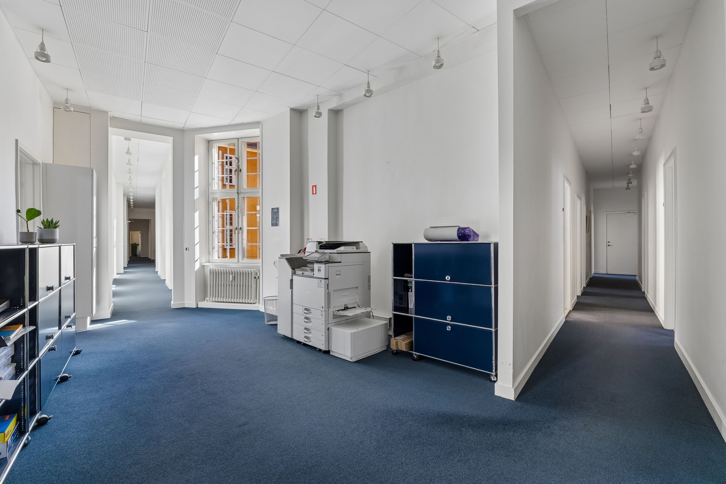 Kontor til leje på Ny Vestergade 17 i København med lyse, neutrale farver og moderne møbler, inklusive printere og højre filehylde.