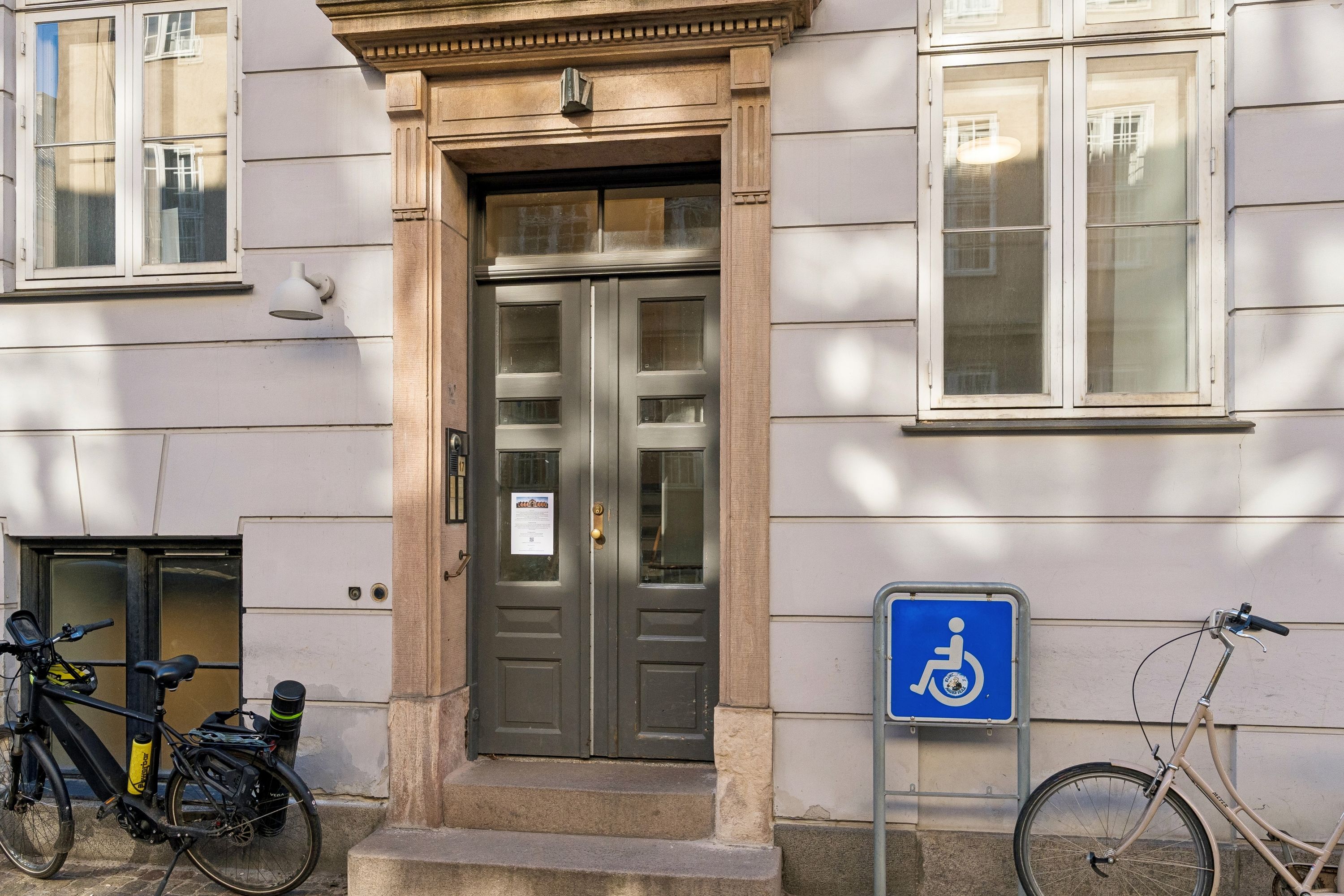 To cykler parkeret foran kontordør med handicaptegn, vinduer med hvide rammer og et lys over døren