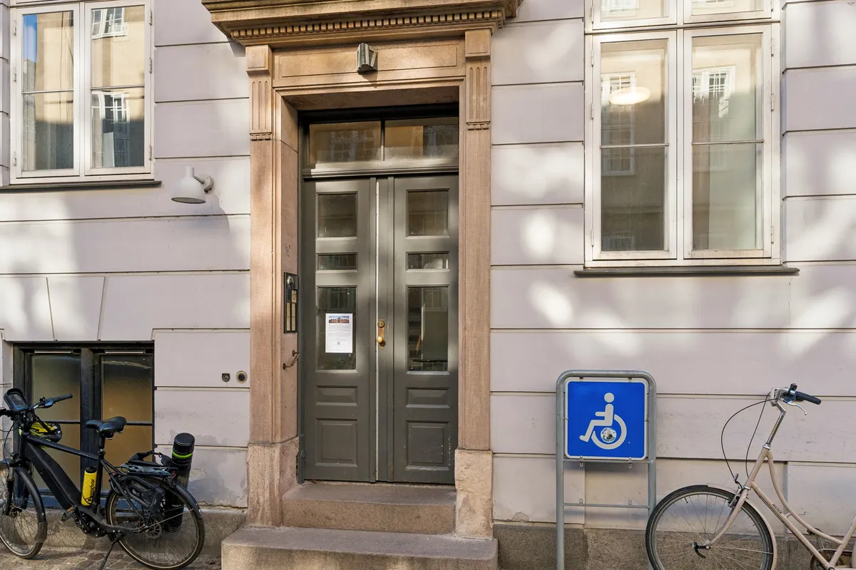 To cykler parkeret foran kontordør med handicaptegn, vinduer med hvide rammer og et lys over døren