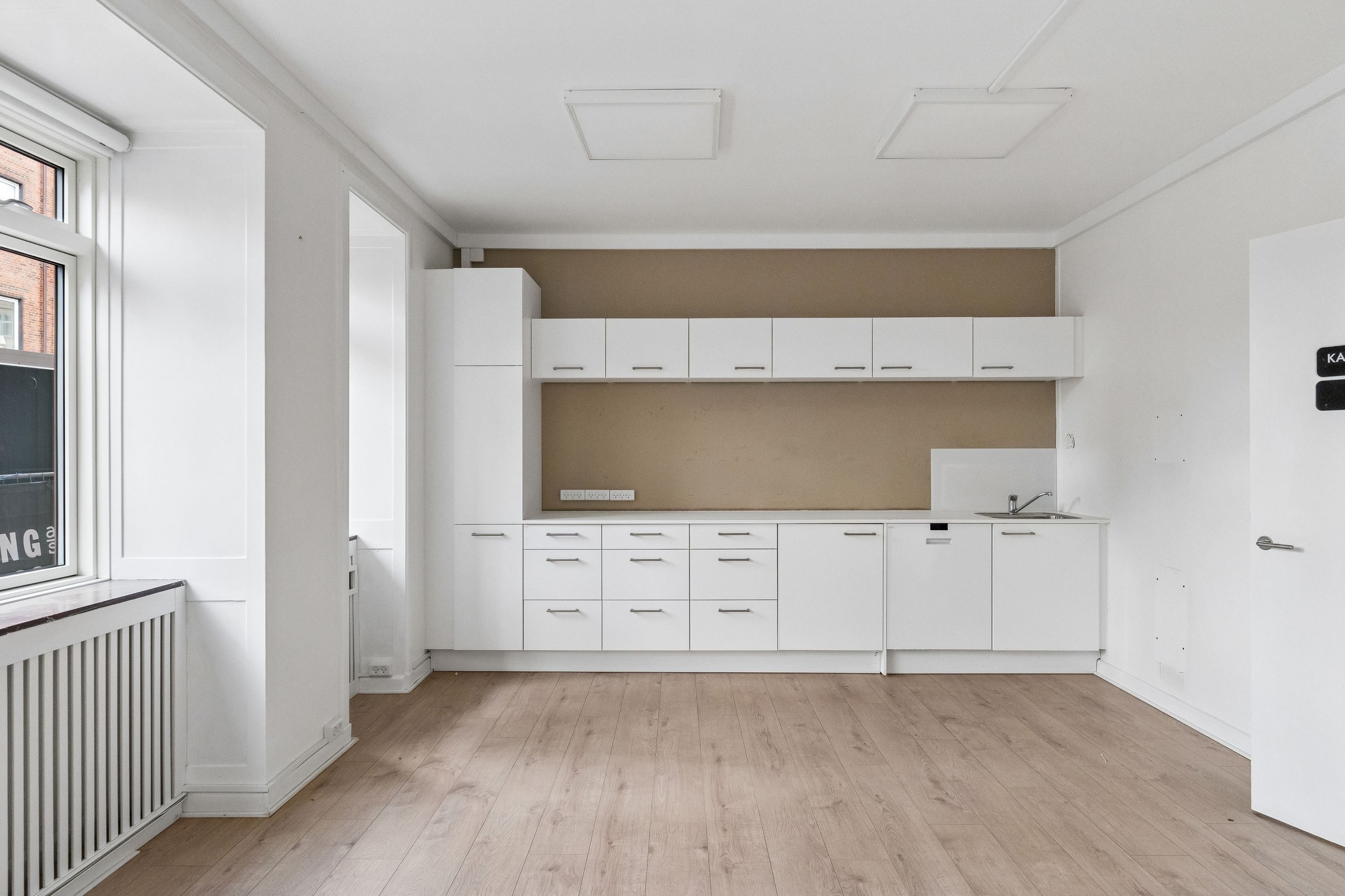 Minimalistisk design med hvidt køkken og lysegult gulv, åbne hylder og vinduer med udsigt til gaderne i København