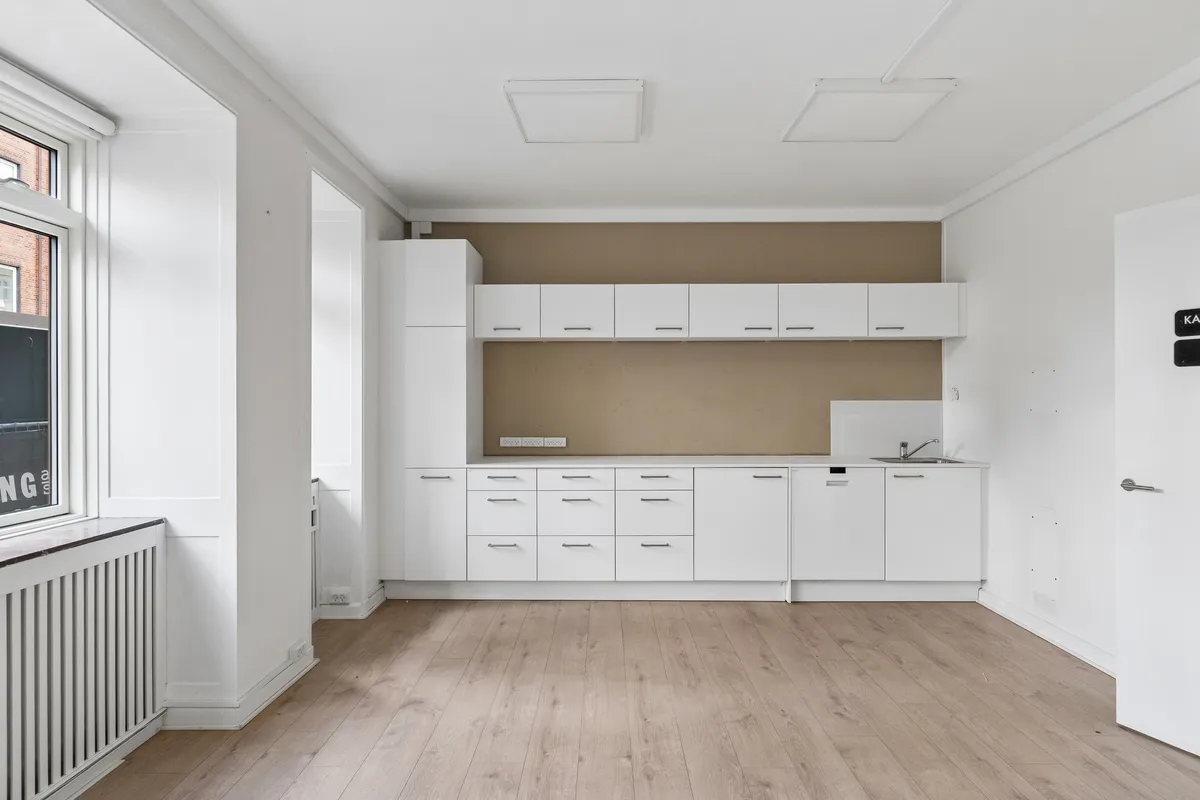 Minimalistisk design med hvidt køkken og lysegult gulv, åbne hylder og vinduer med udsigt til gaderne i København