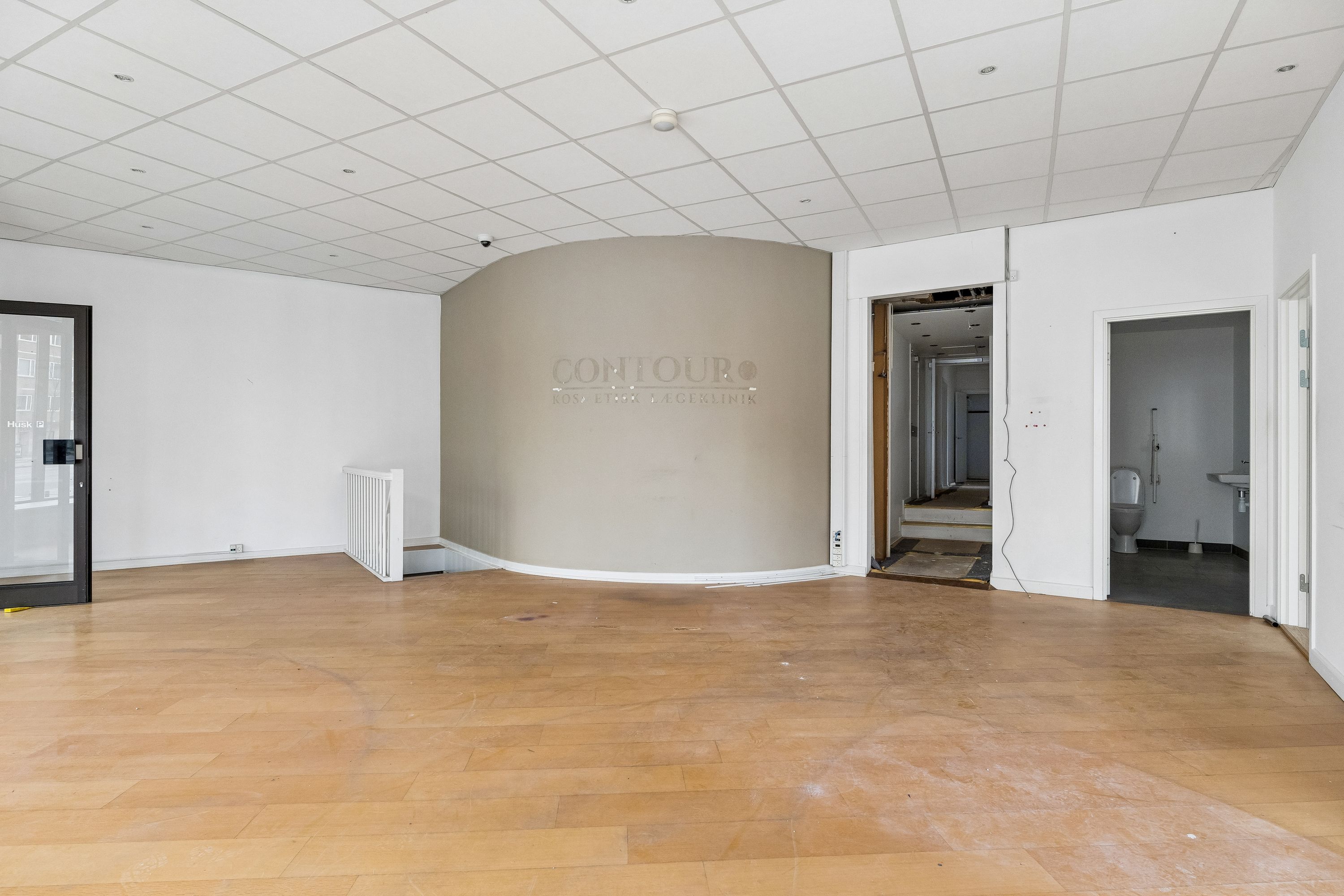 Lej butik i København med stort hjørnerudervindue og luksuriøs indgangsdør. Bagved er toiletrum og adgang til kælder.