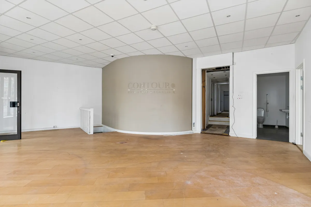 Lej butik i København med stort hjørnerudervindue og luksuriøs indgangsdør. Bagved er toiletrum og adgang til kælder.