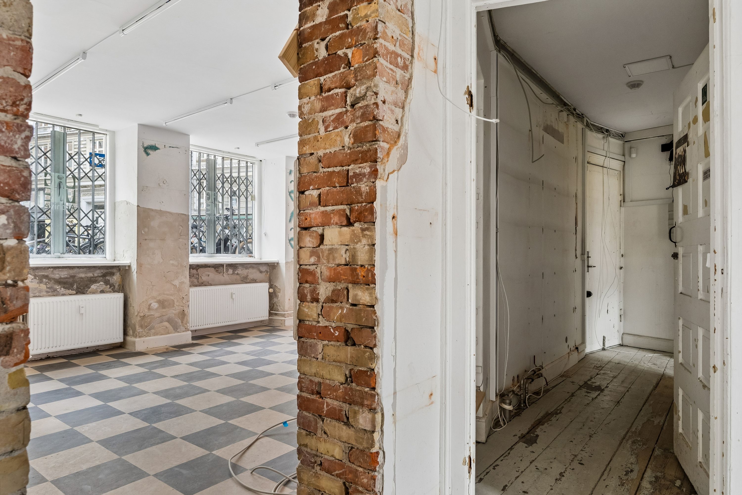 Lej en butikslokal på Birkegade med søjler og loftsbøjler i røde mursten og loftsbjælker samt et slettet gulv med mønstret trægulv