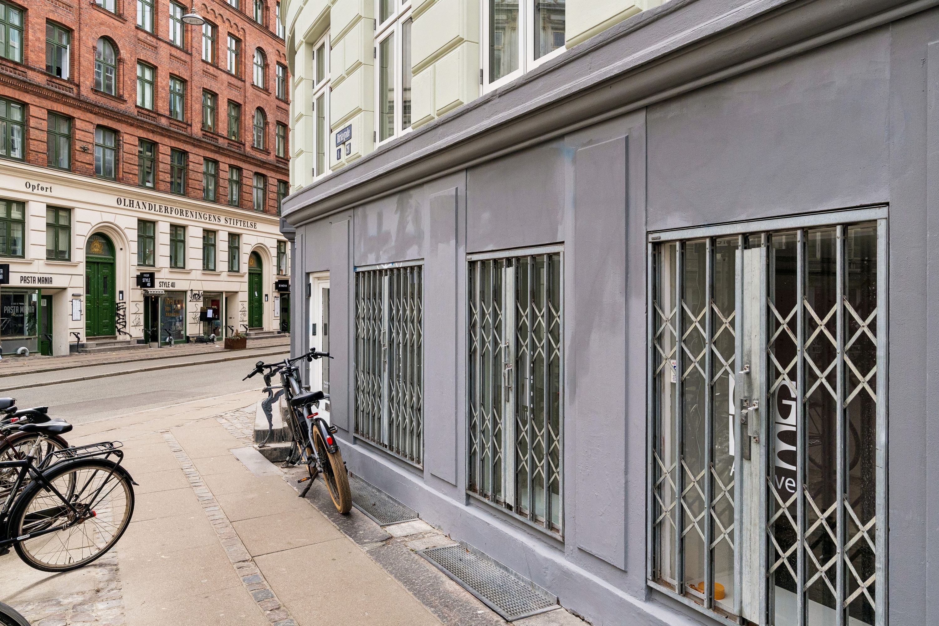 Bygning med glasruder og metalruder og cykler parkeret i forkant og gadens fortov med en gul linje og en røgdetegning