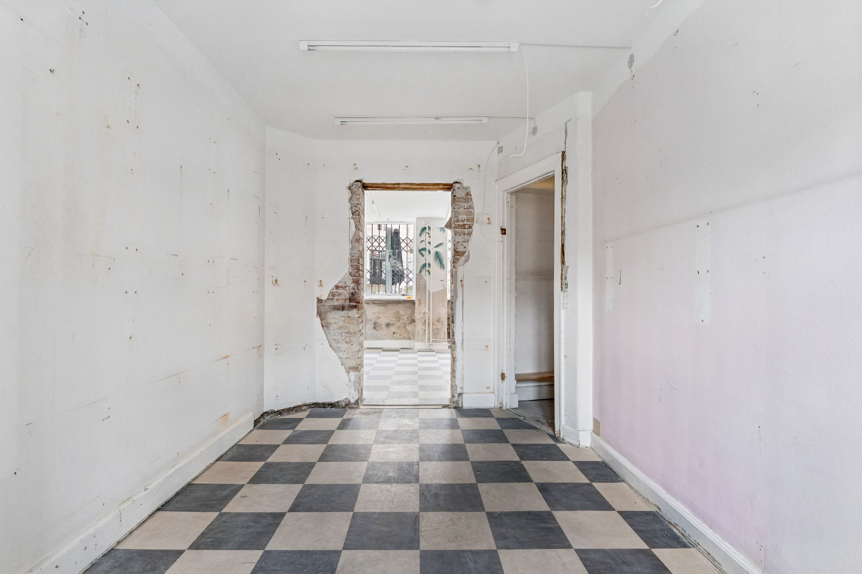 En stor, tom og renoveringsvenlig butik med tømmerloft og trægulv og åbne døre til et gårdrum med terrasse