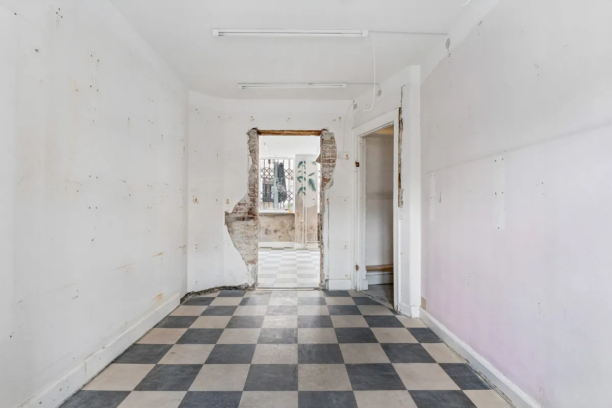 En stor, tom og renoveringsvenlig butik med tømmerloft og trægulv og åbne døre til et gårdrum med terrasse