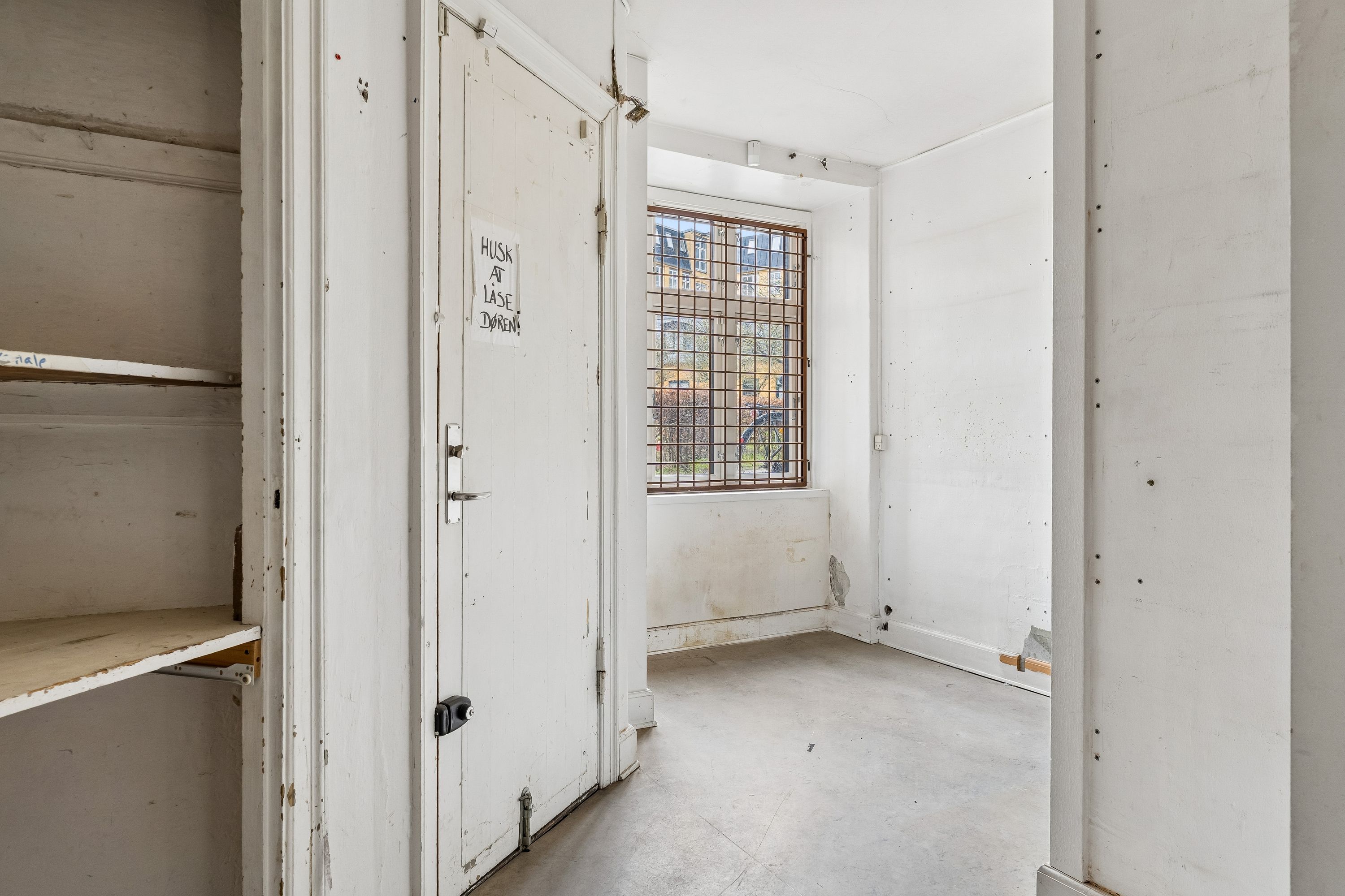 Et tomt rum med åbne døre og et vindue med gitter og en skilt med tekst på en hvid væg