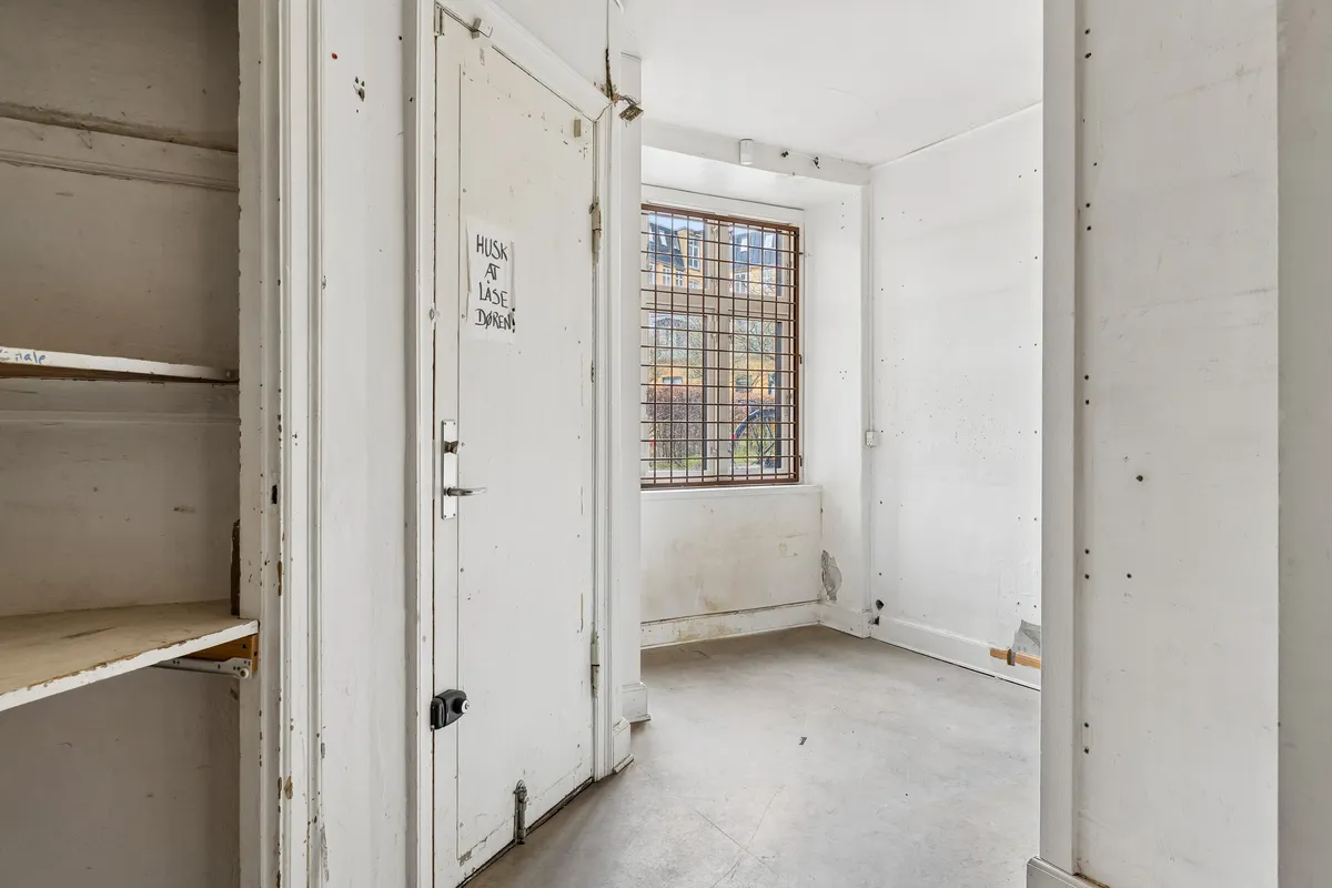 Et tomt rum med åbne døre og et vindue med gitter og en skilt med tekst på en hvid væg