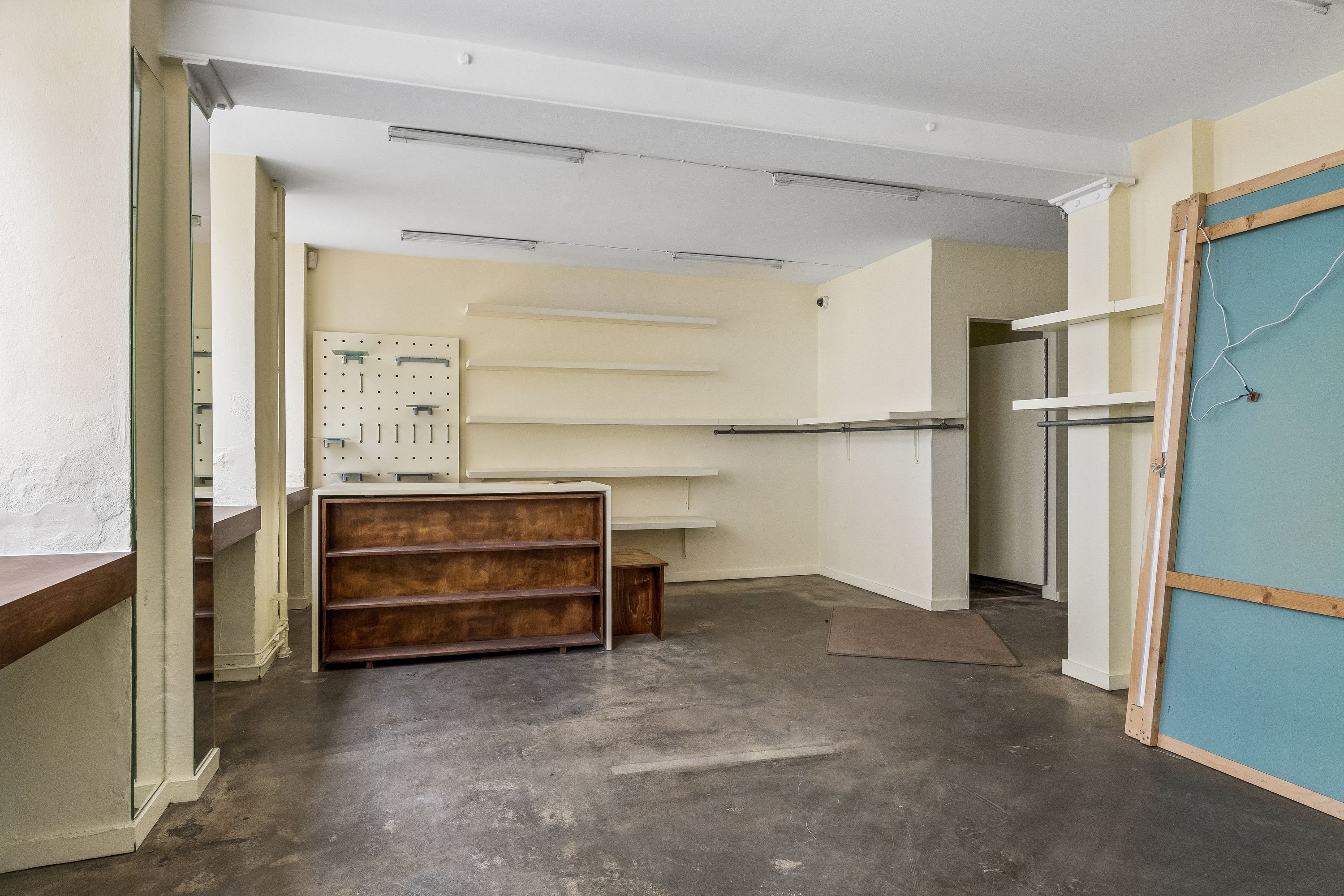 Et stort, åbent rum med lyse vægge og højloft, en gulvbeslag og to høje, lyse hylder. Et træskab med højloft og en håndfuld hængehylder