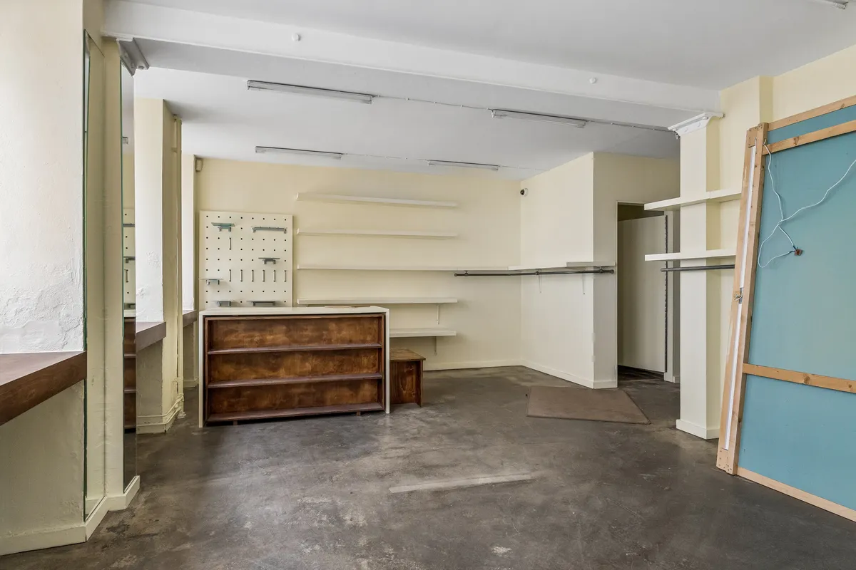 Et stort, åbent rum med lyse vægge og højloft, en gulvbeslag og to høje, lyse hylder. Et træskab med højloft og en håndfuld hængehylder