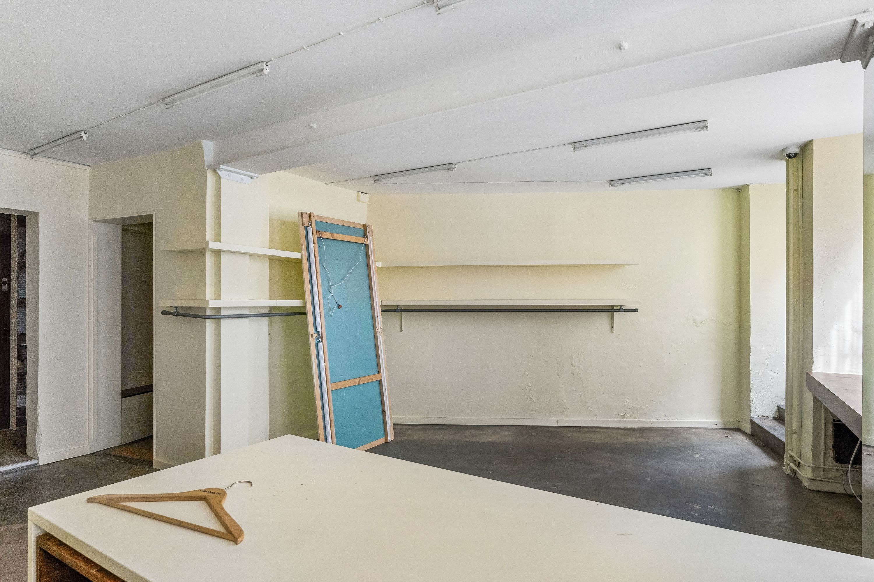 Lukket handelslokal med hængeklæder og lyse hælvede på bordet og hvidt loft med indbyggede lys.