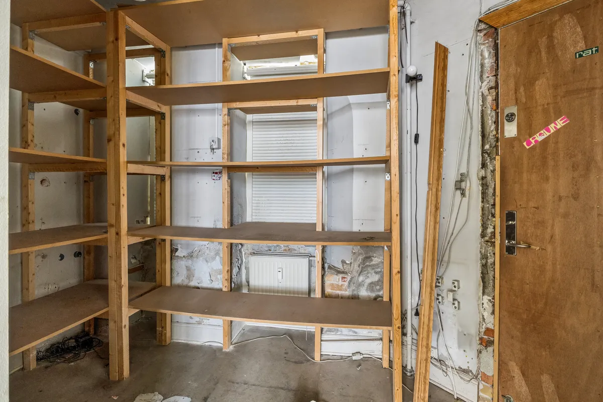 Lejlighed med flere hylder og ledningsforløb i gården i Nørrebro med åbne døre og lysepunkter