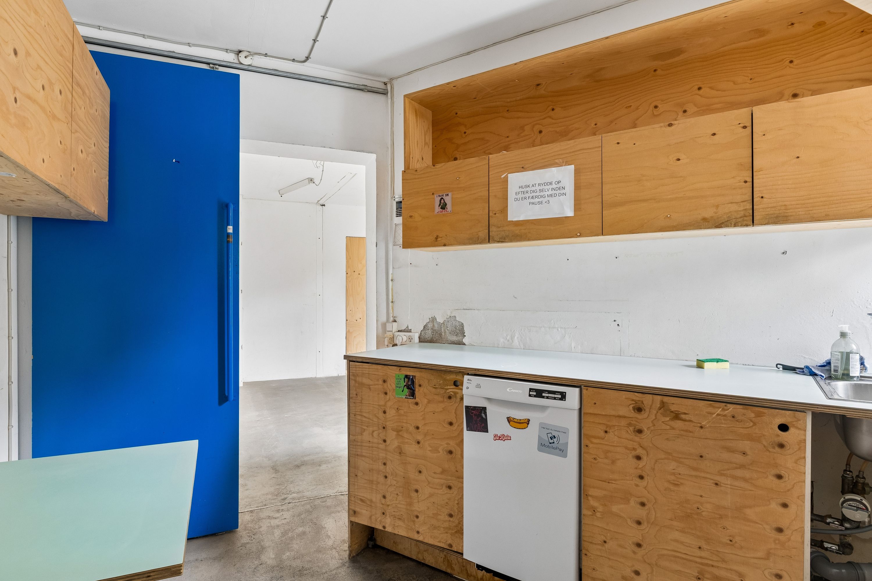 Køkken med lysegrå hætte og lyseblå væg. Rent og pænt med moderne design og lyse trækabinetter. Skrive på væggen og rengøringsmiddel på bord.