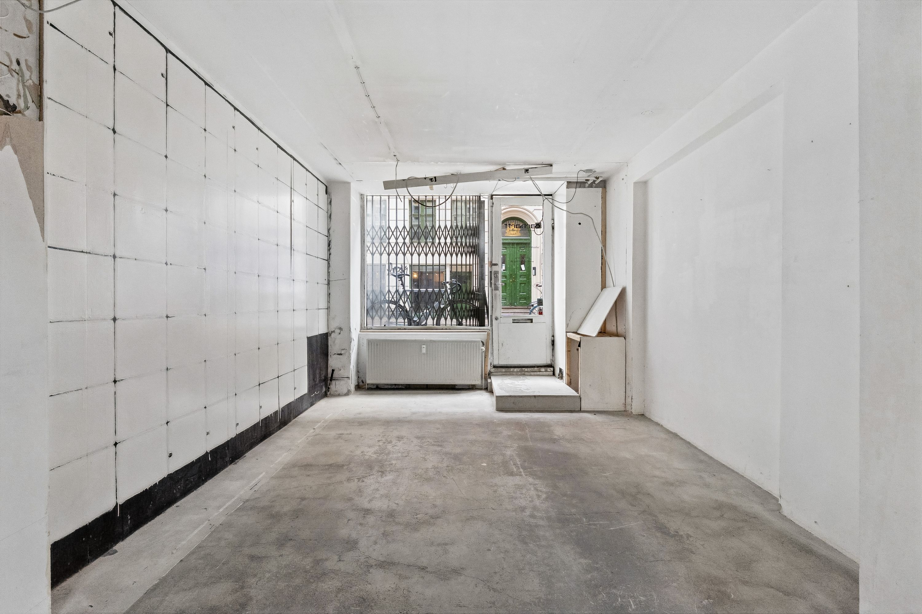 Store, hvide vægge og en gulvbelægning af beton i en tom lejlighed med vinduer og døre til gade