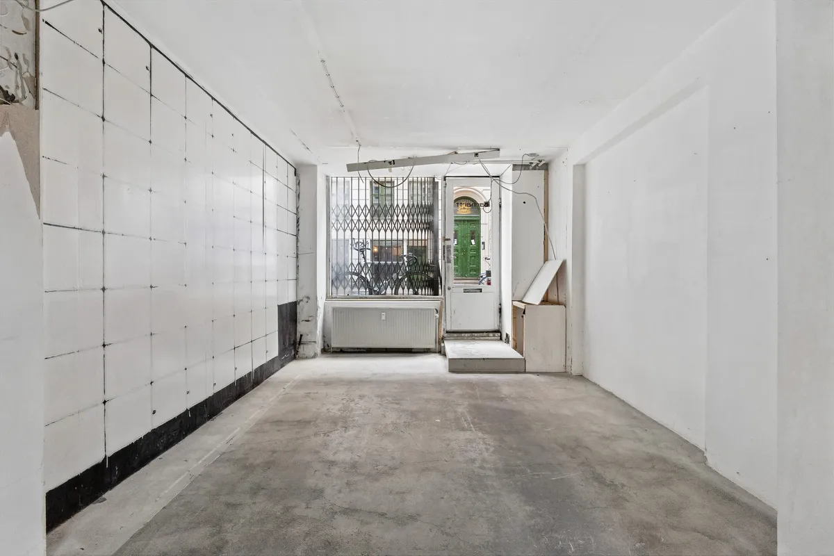 Store, hvide vægge og en gulvbelægning af beton i en tom lejlighed med vinduer og døre til gade