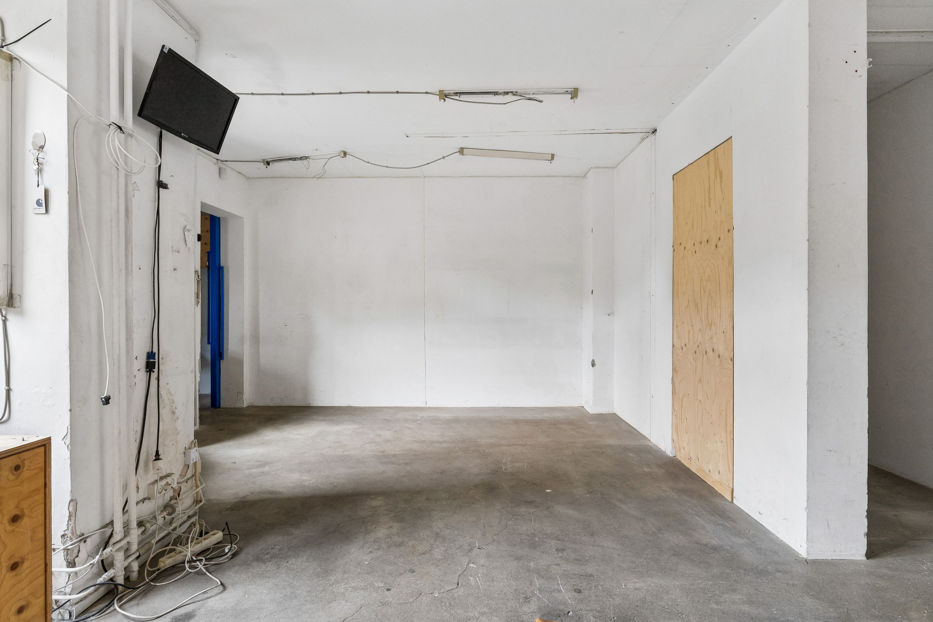 En stor og rummelig værkstedslokal med hvide vægge, en kabelforsyning og et fjernsyn i loftet