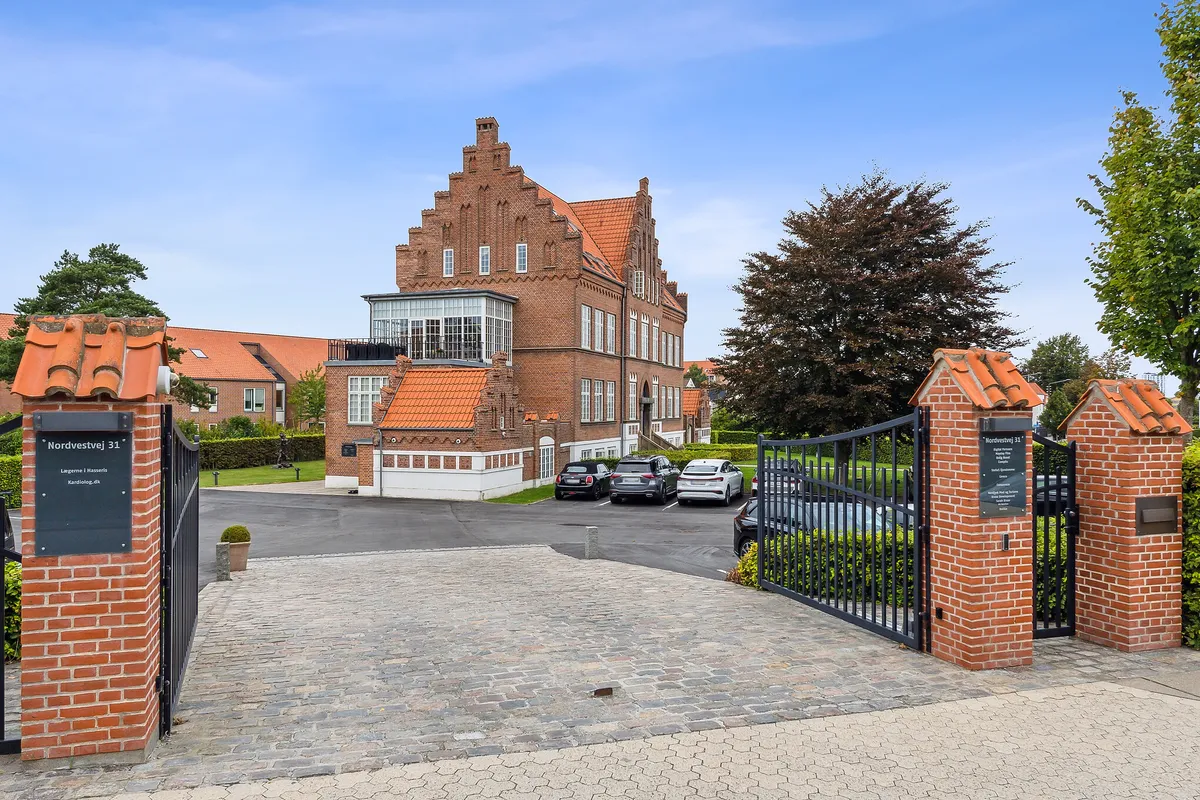 Kontor eller skrivebord i eksklusive rammer på Nordvestvej 31 i Aalborg med parkeringsplads og grønne træer og buske. Et moderne bygning med røde tag og hvide vindueskarm.