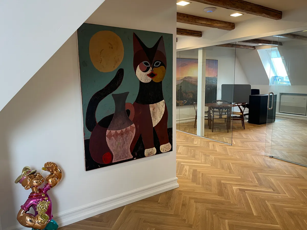 Kontorlokaler med loftsrum og lyse loftstræer, hvor der er maleri med kat og vase og gulvtæppe