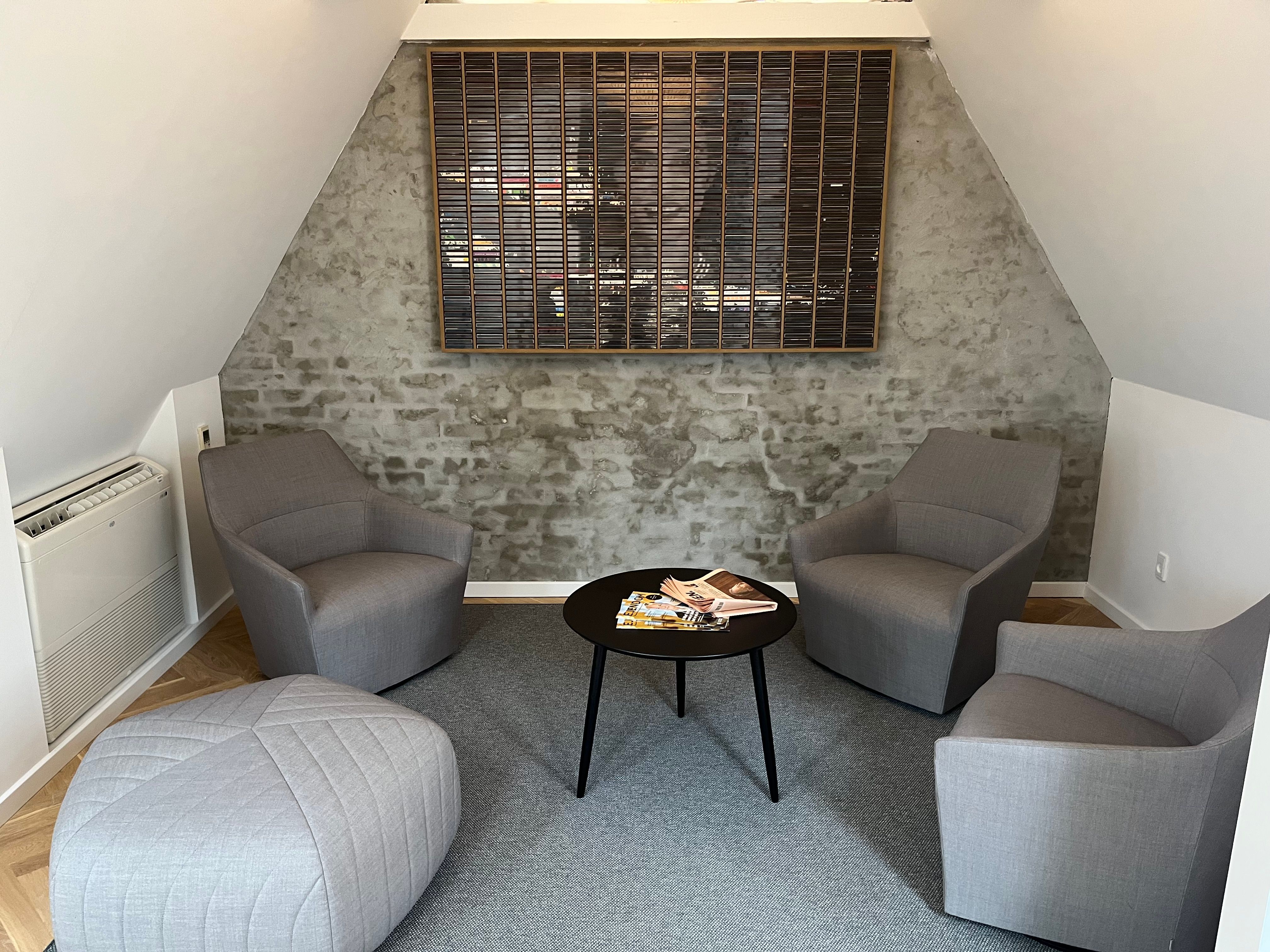 Minimalistisk kontor med lyse, grå møbler og en rund, sort bord med tidsskrifter. Moderne loft og højt til loftet med lyserøde gulvbelægning og et kunstværk på væggen