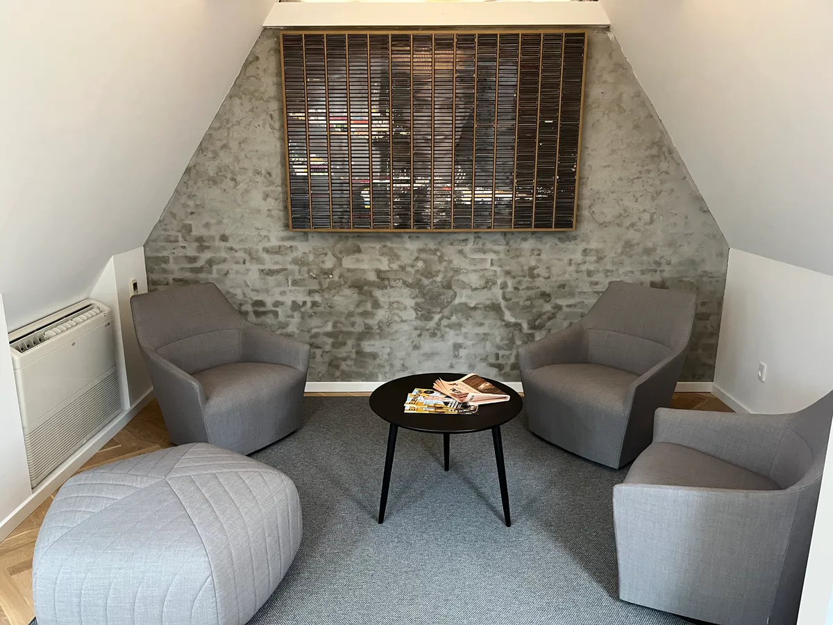 Minimalistisk kontor med lyse, grå møbler og en rund, sort bord med tidsskrifter. Moderne loft og højt til loftet med lyserøde gulvbelægning og et kunstværk på væggen