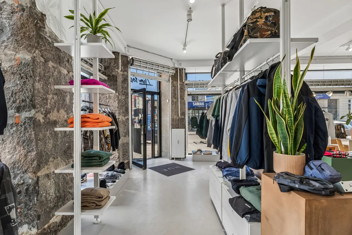 Butik med klædtøj og sko i hvidt og blåt og to store gulvvægge med grønne planter i lysebrune potter og lysekroner på loftet