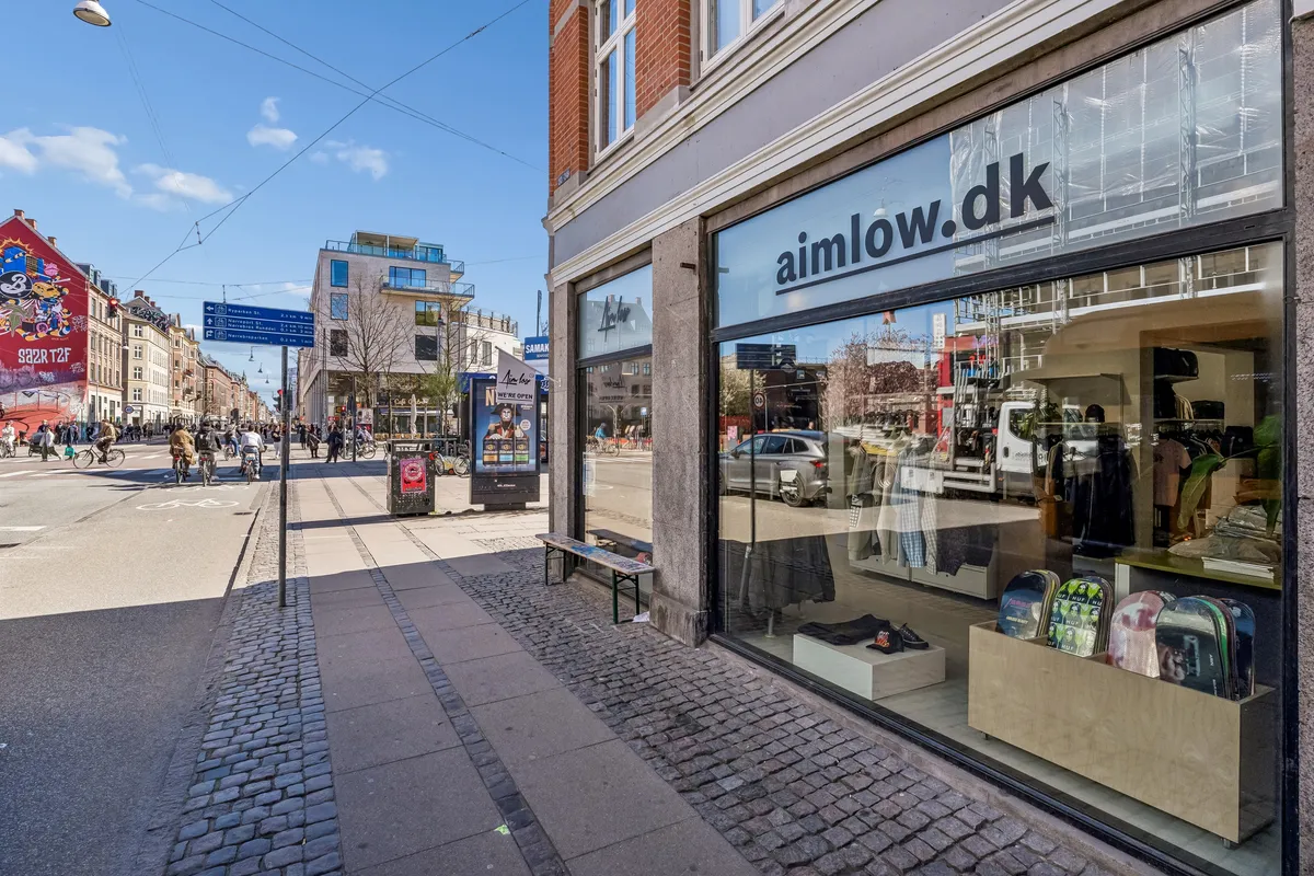 Butiksvindue med skateboards og tøj, skrift "aimlow.dk", solskin på asfalt og folk går på cykler og går på gågade
