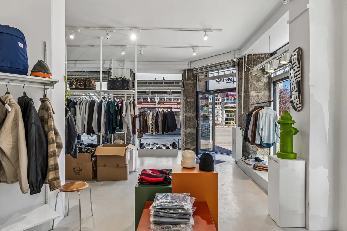 En butik med tøj og sko samt møbler og sportsudstyr i et lyst og velorganiseret interiør med grønt vandhane og lysekroner i loftet