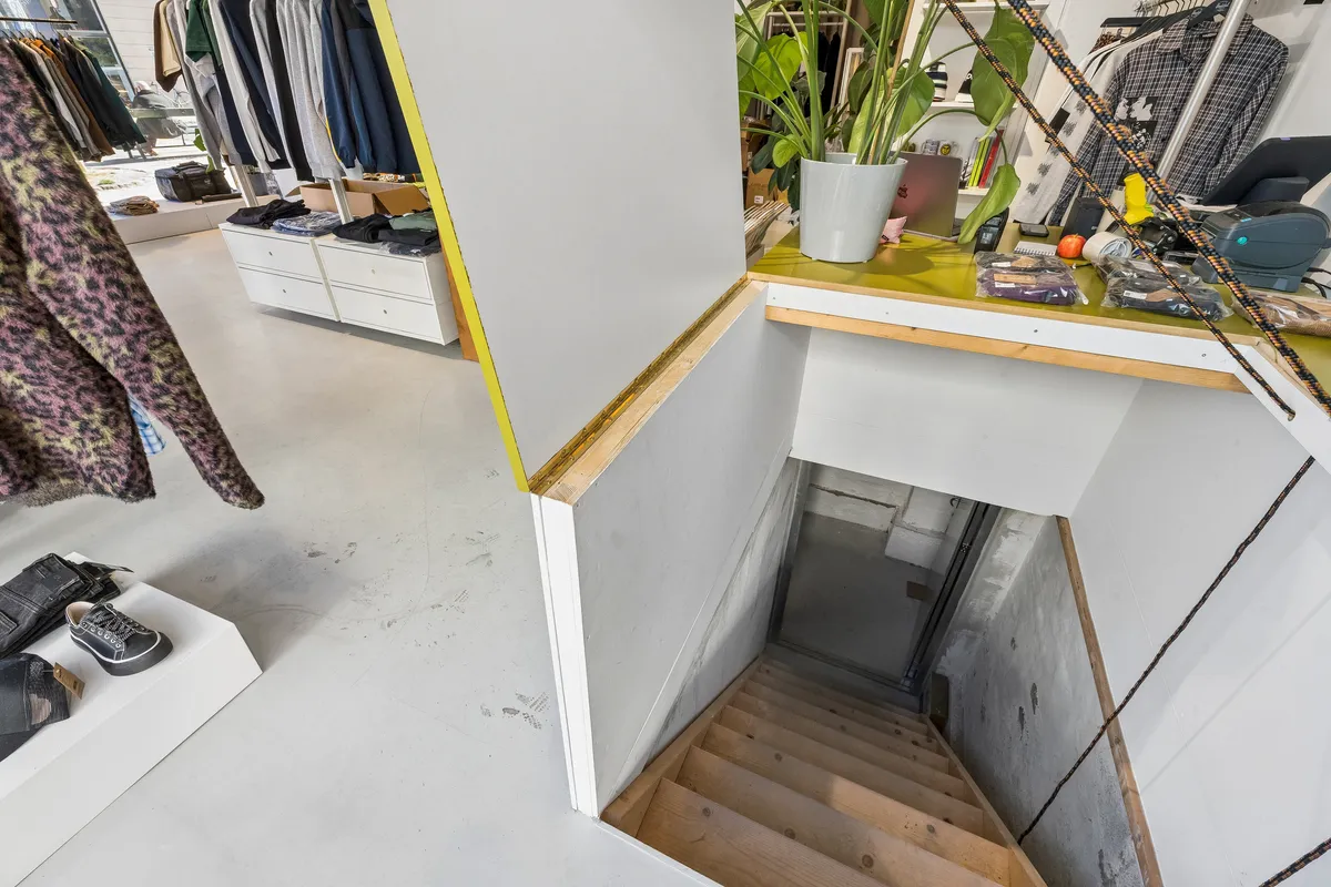 København Nørrebrogade 213A butik til leje, hvor tøj og sko udstilles, og der er et skab med bøger og ting, en plante i en vase og en stige til kælderen