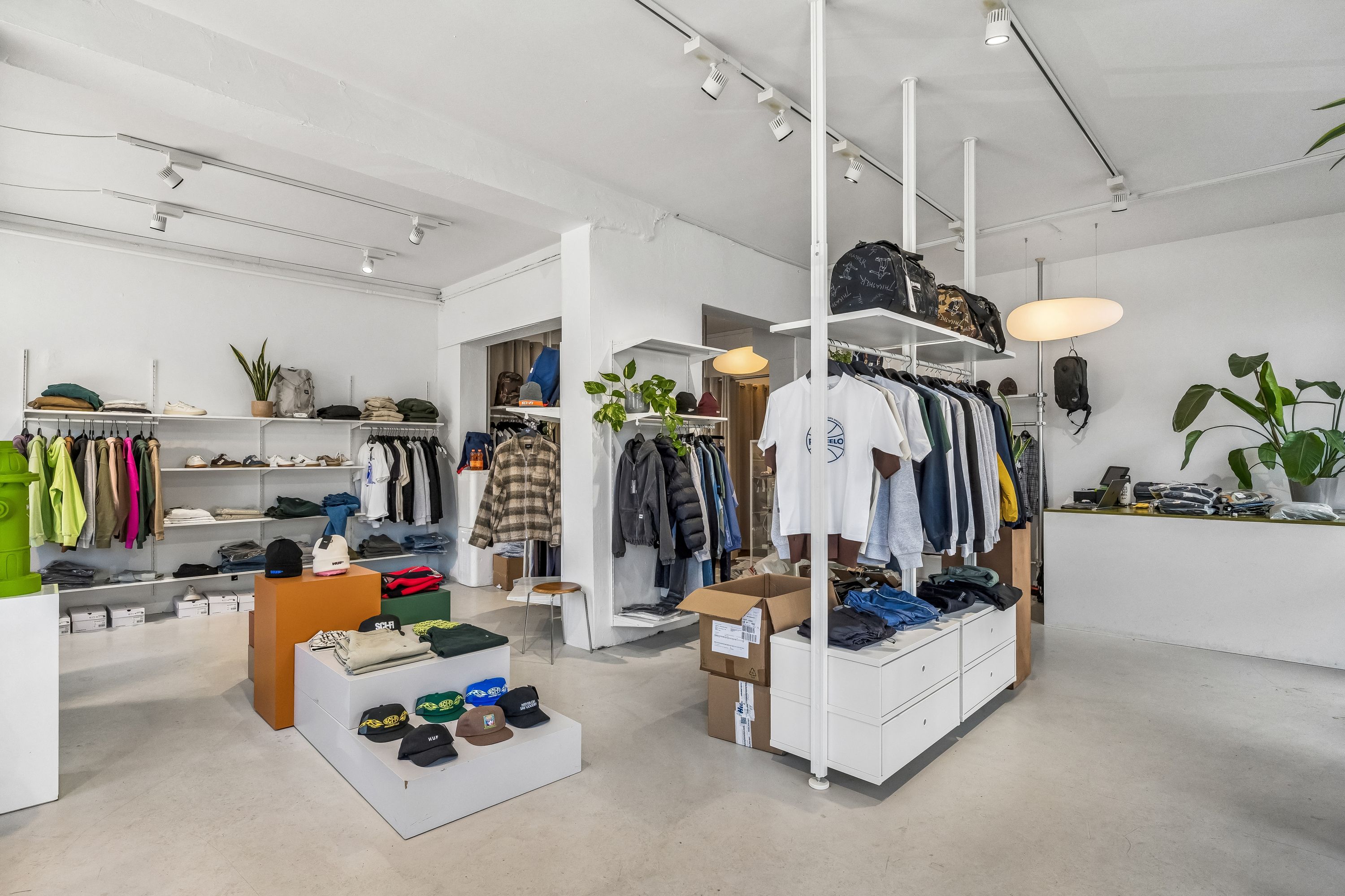 Nymøbleret og veludstyret butik med højt til loftet og moderne indretning. Møbler, klædeskabe, hylder og tekstiler er i hvidt og gråt. Et stort gulvspejl reflekterer rummets indretning