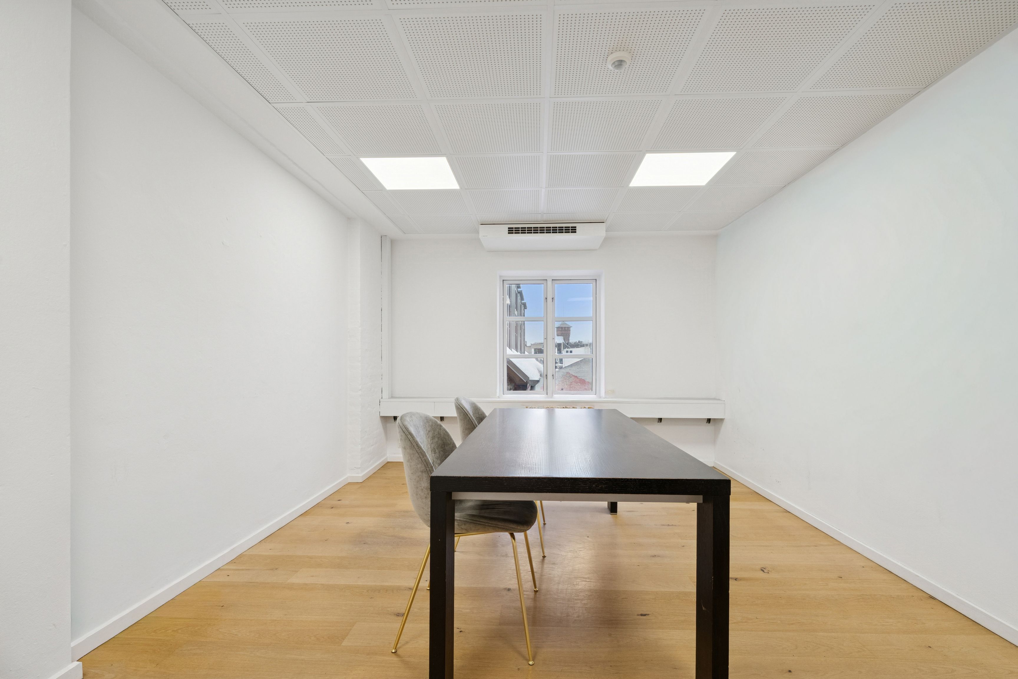 Et kontorlokal med højt til loftet, hvidt malet vægge, moderne møbler, gult gulv og et stort vinduesparti. Et spændende lejemål med udsigt til Gammel Strand metro.