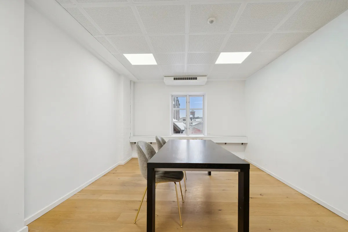 Et kontorlokal med højt til loftet, hvidt malet vægge, moderne møbler, gult gulv og et stort vinduesparti. Et spændende lejemål med udsigt til Gammel Strand metro.