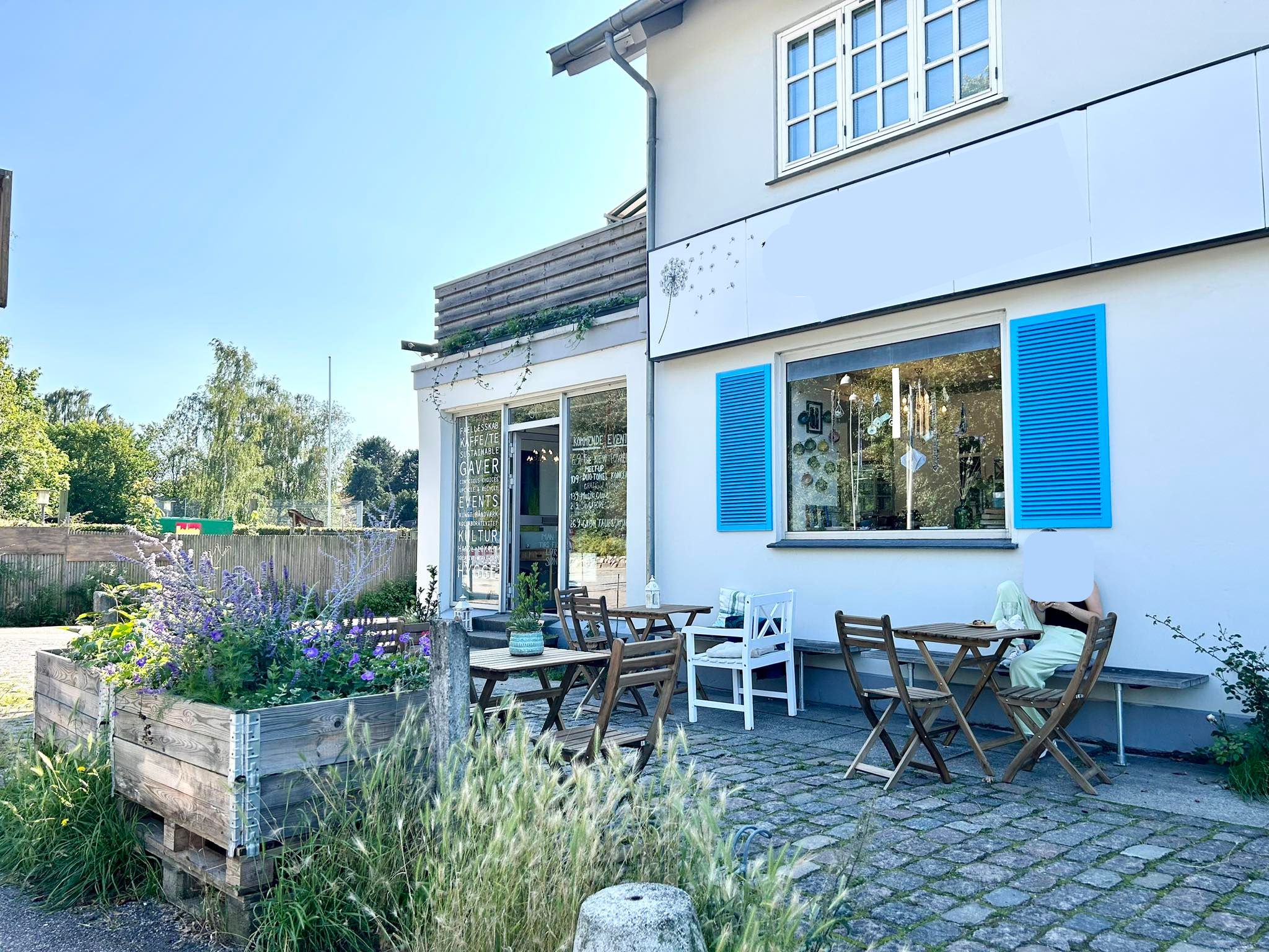Kontor til leje i Kongens Lyngby med udsigt til have. Lyst kontorlokaler med terrasse og blomster. Hvid murstensbygning med blå rudefløje og grønt tag.