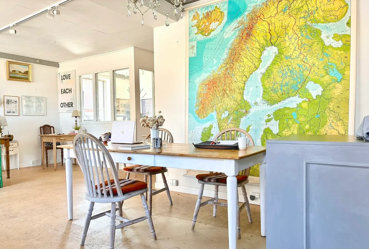 Kontor med loftslampe og gult, grønt og rød kort. Bord med papirvægge og røde kufferter og puder. Bord med blomster og lysestage.