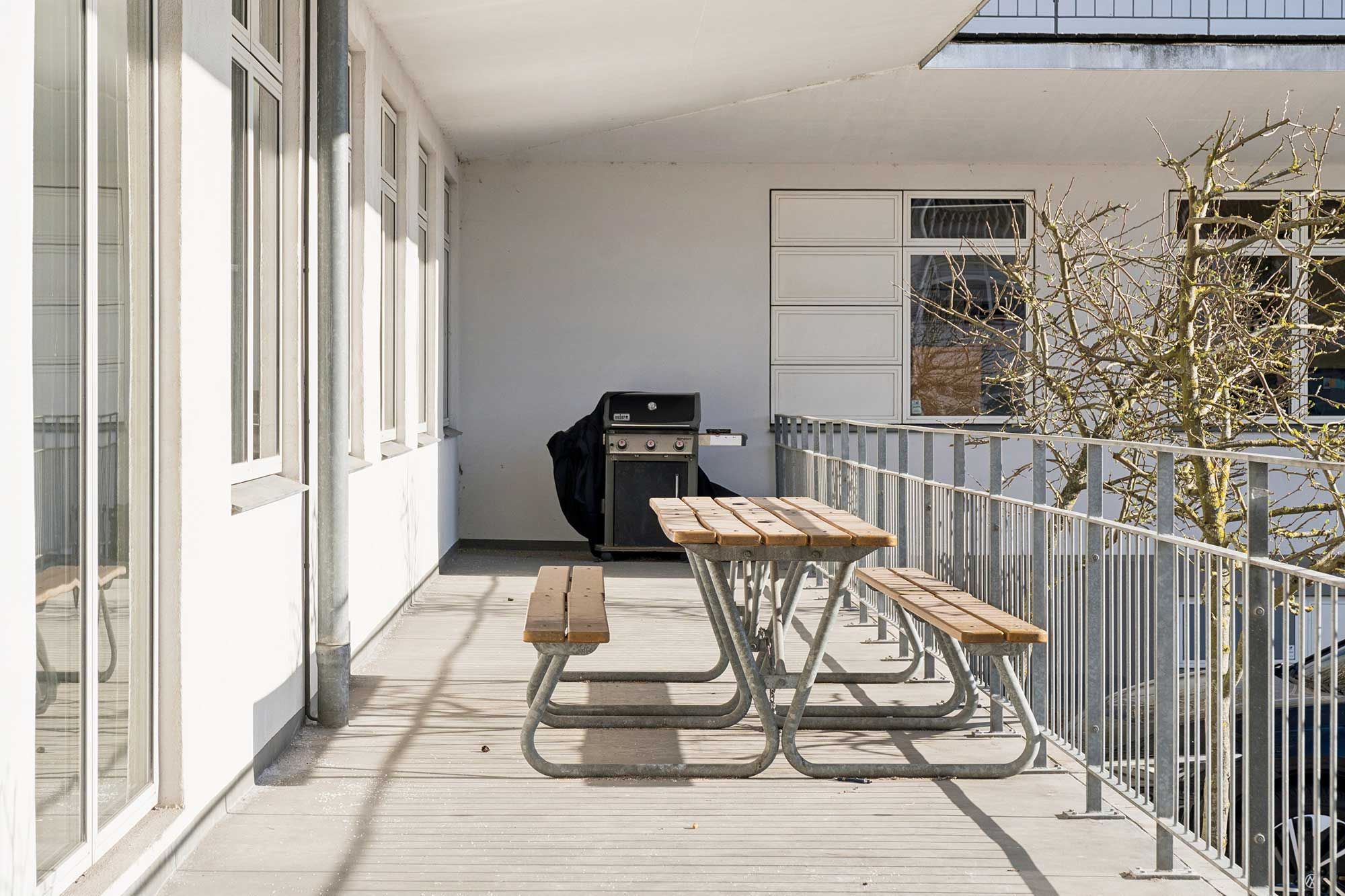 Lyst kontorlejemål med grill og bord og bænke på balkonen. Der er et grill på balkonen og en stang af metal.