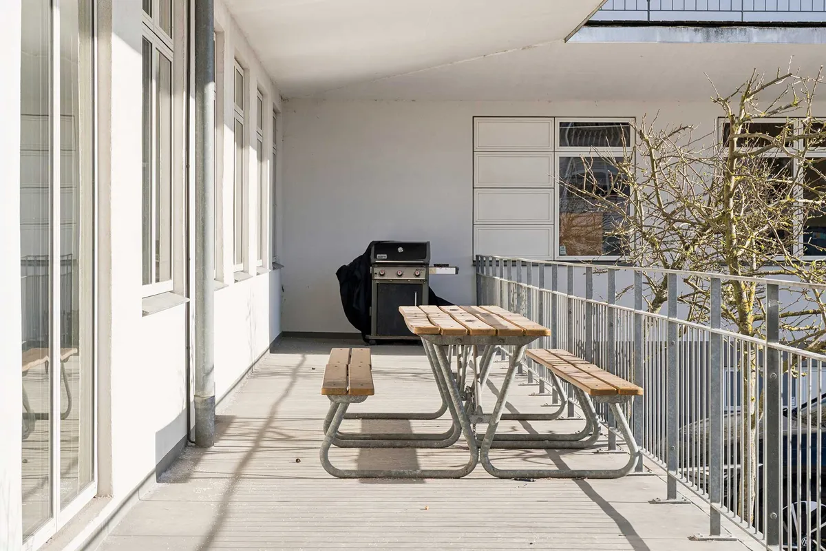 Lyst kontorlejemål med grill og bord og bænke på balkonen. Der er et grill på balkonen og en stang af metal.