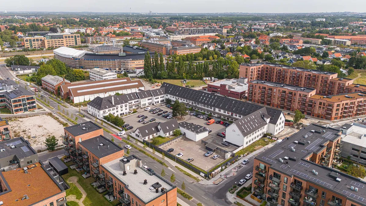 Lyst kontorområde med industrielle undertoner og adgang til fælles kantine og parkering. Bygningerne har mange vinduer og solceller på tag.