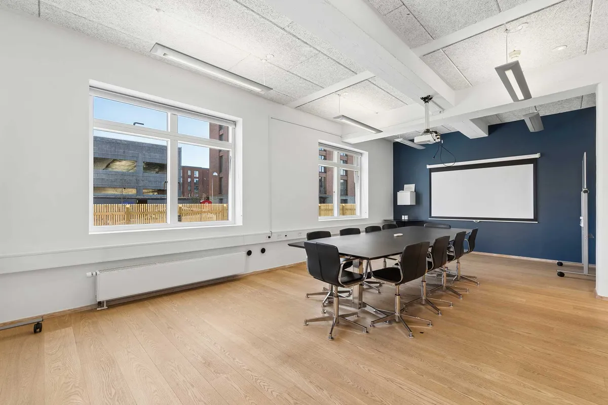 Kontorlokaler med lyse vinkler og moderne design, hvor mødesalen er indrettet med skrivebord, stole og hvide vægge