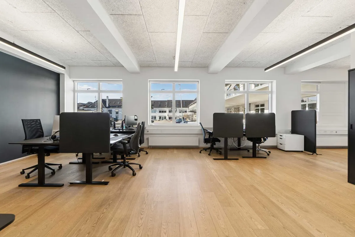 Kontorlokaler med lyse vinduer og moderne møbler og gulvbelægning. Kontorer med moderne skrivebord og stol. Vægge med mørke farver og hvide loftsbjælker.