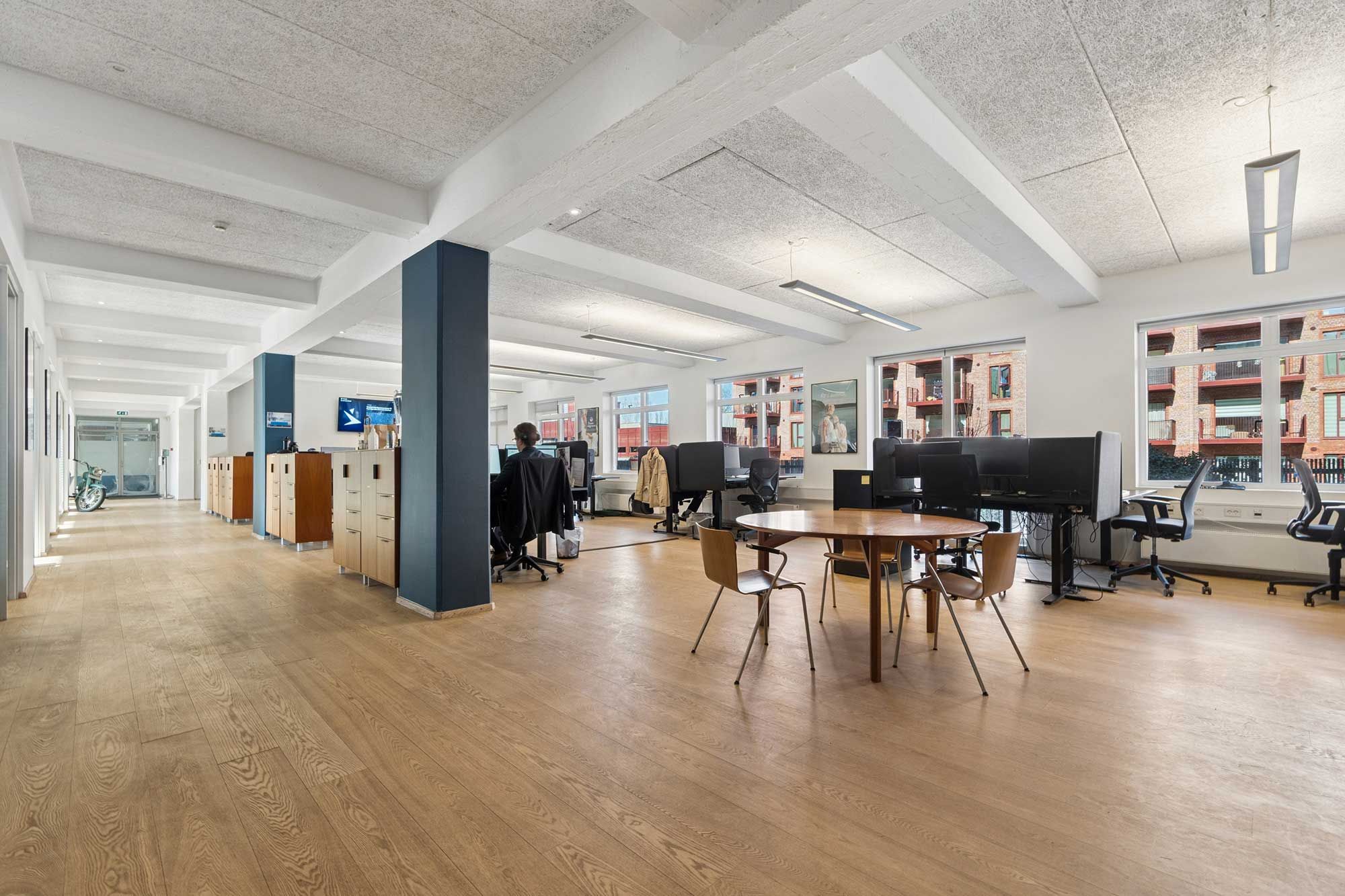 Kontorområde med åben gulvplan og lyse lofter, skriveborde og computere, samt møbel og cykel ved siden af døren