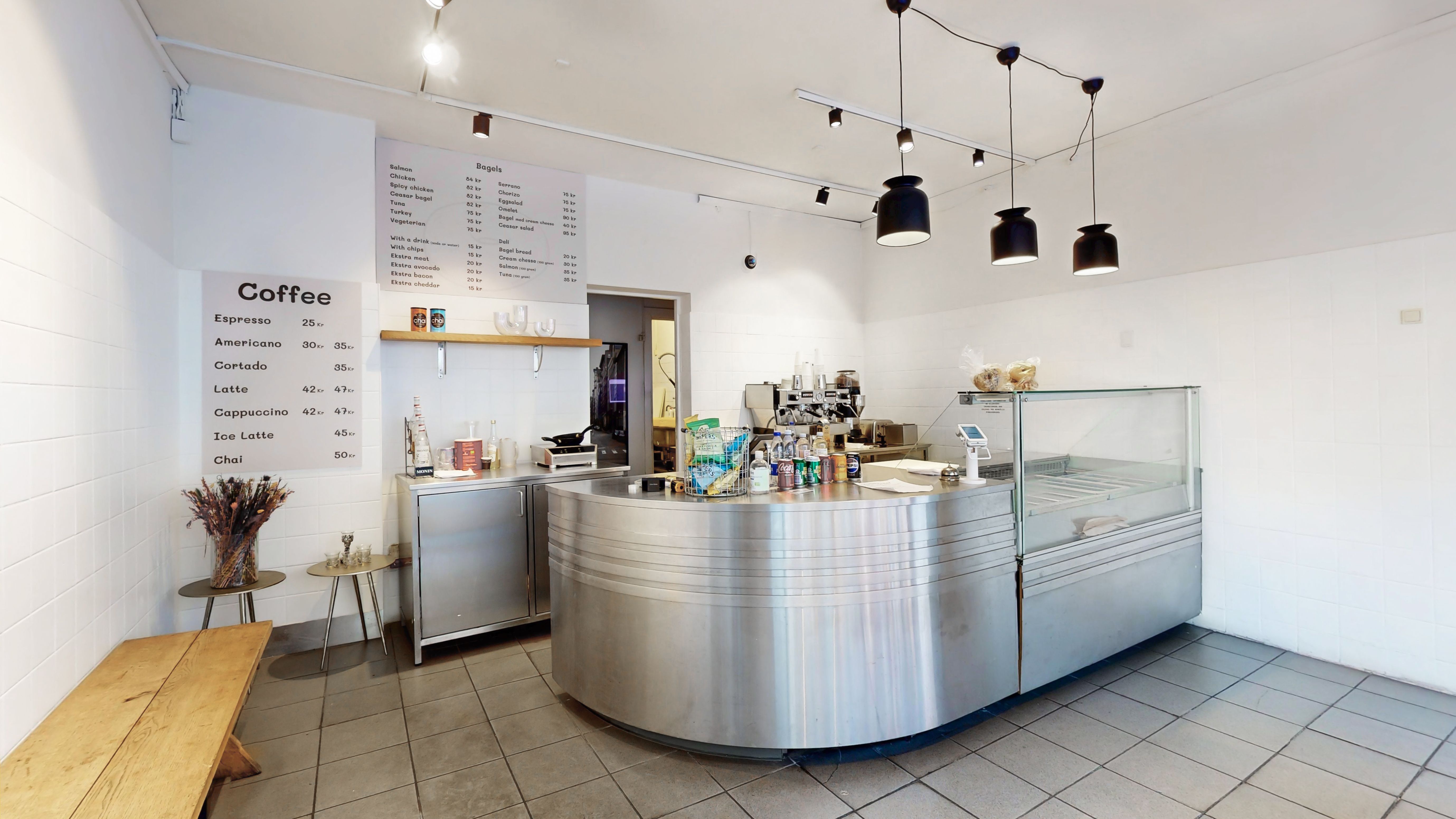 Værelse med menu og prisliste, køkken med apparater, øl og drikkevarer, skab med glasdør og træbord med blomster.