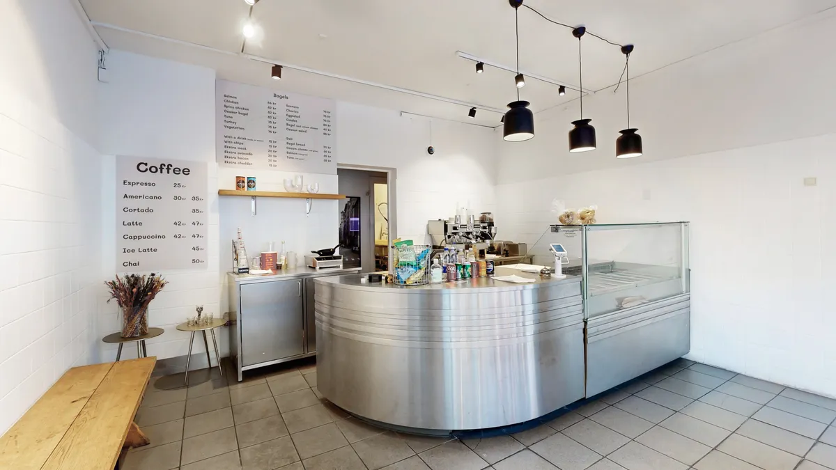 Værelse med menu og prisliste, køkken med apparater, øl og drikkevarer, skab med glasdør og træbord med blomster.