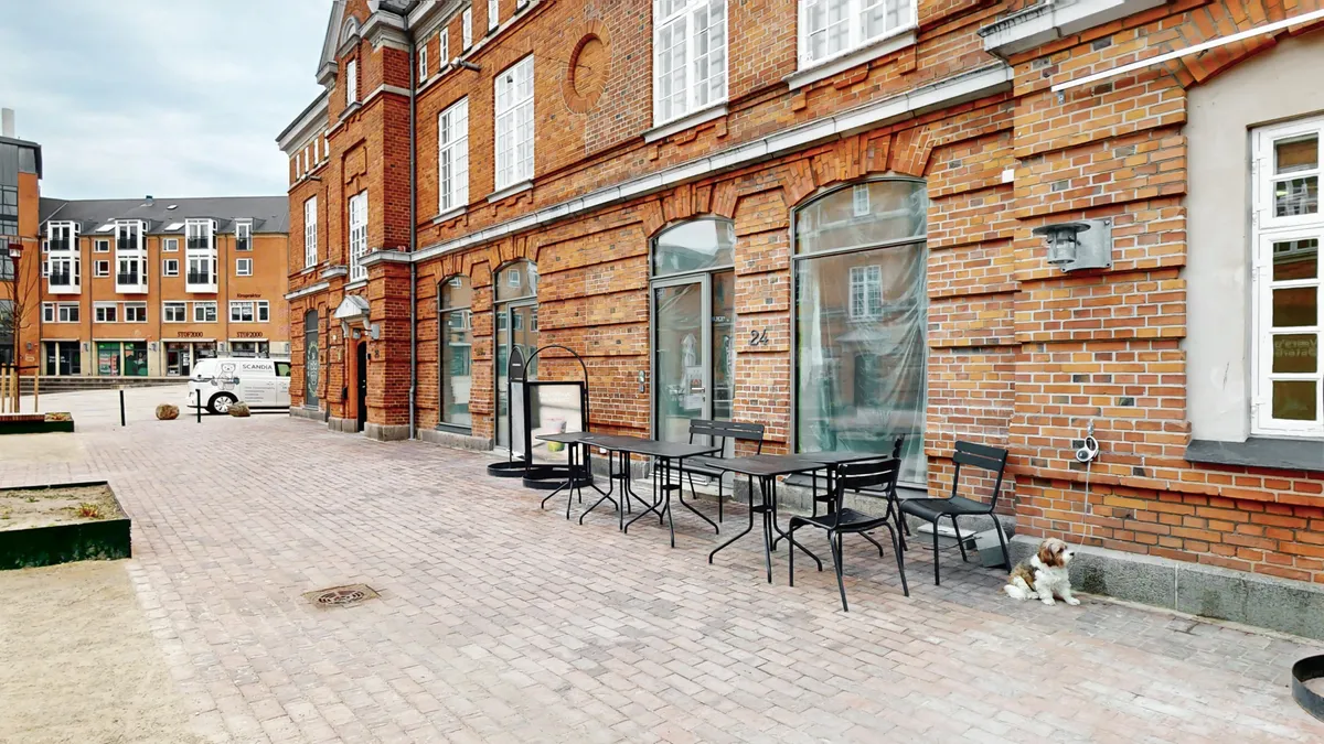Lyst erhvervslejemål med terrasse i København Ø. En stor terrasse med spisesteder og stolpelys foran. En søt hvalpe snor rundt foran døren til et moderne kontor