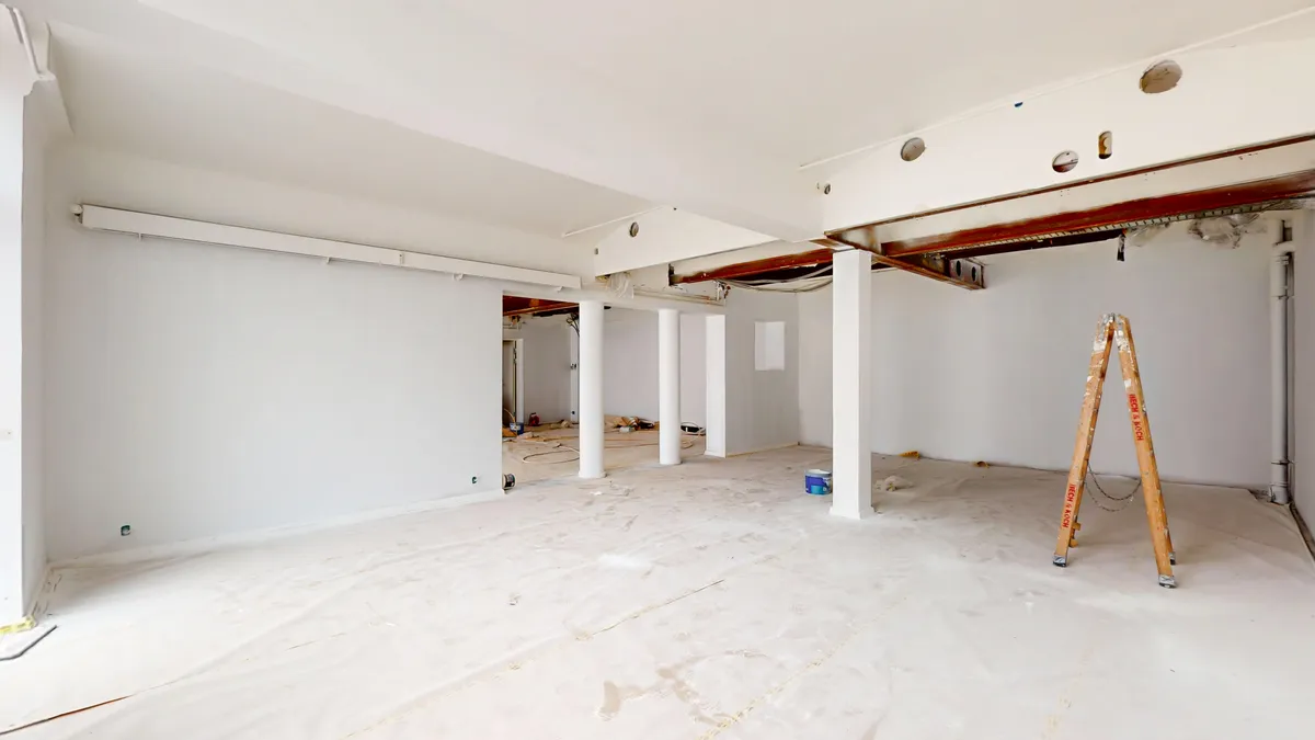 Lyst og rent erhvervslokale med hvide vægge og gulv, og en stige med malingsfadet på gulvet